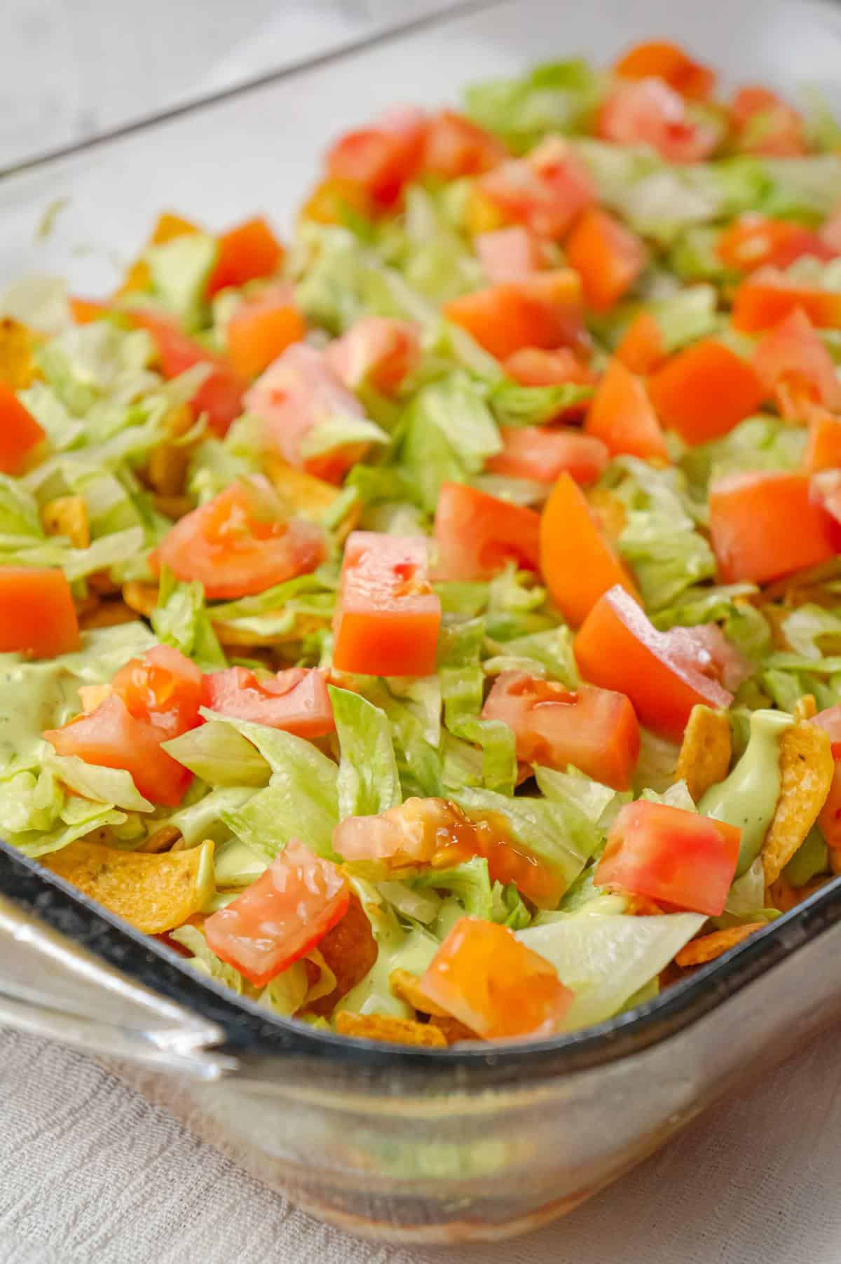 Chicken Taco Frito Pie is an easy weeknight dinner recipe made with shredded chicken tossed in salsa, taco seasoning and chili sauce and topped with cheese, Fritos corn chips, avocado dip, shredded lettuce and diced tomatoes.