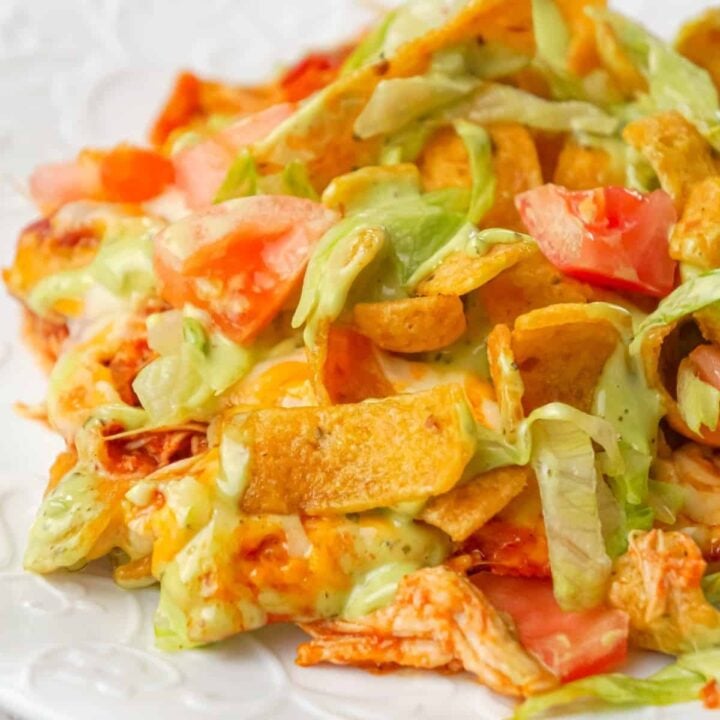 Chicken Taco Frito Pie is an easy weeknight dinner recipe made with shredded chicken tossed in salsa, taco seasoning and chili sauce and topped with cheese, Fritos corn chips, avocado dip, shredded lettuce and diced tomatoes.