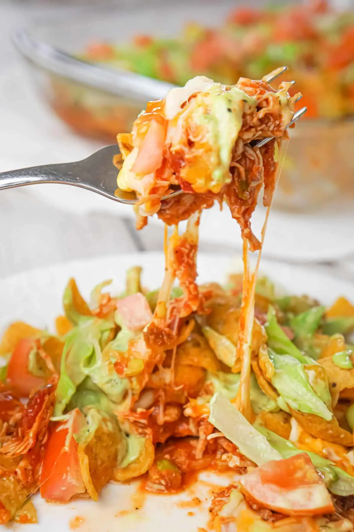 Chicken Taco Frito Pie is an easy weeknight dinner recipe made with shredded chicken tossed in salsa, taco seasoning and chili sauce and topped with cheese, Fritos corn chips, avocado dip, shredded lettuce and diced tomatoes.