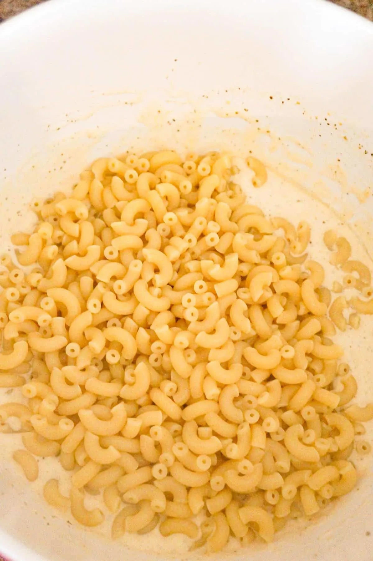 cooked macaroni noodles on top of creamy sauce mixture in a mixing bowl