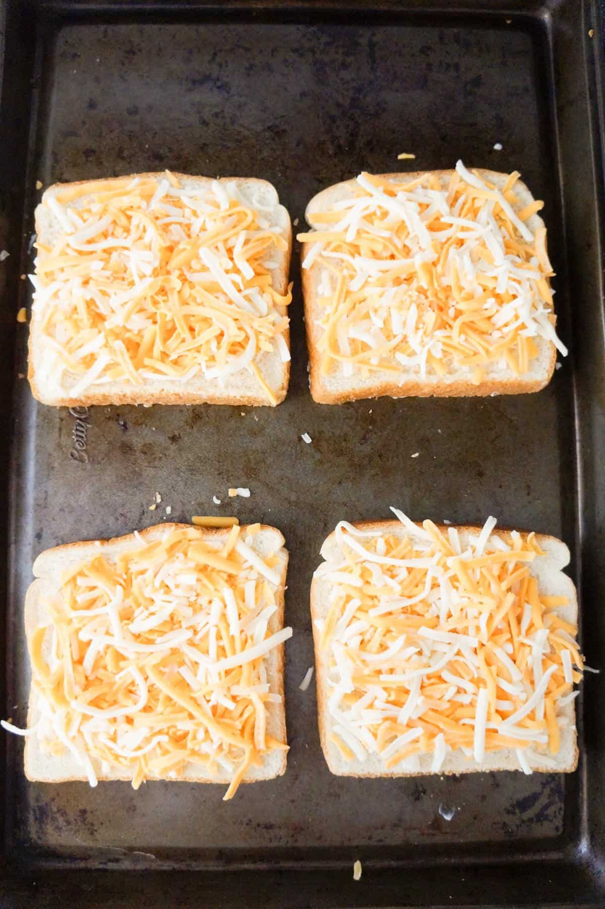 shredded cheddar cheese on top of bread on a baking sheet