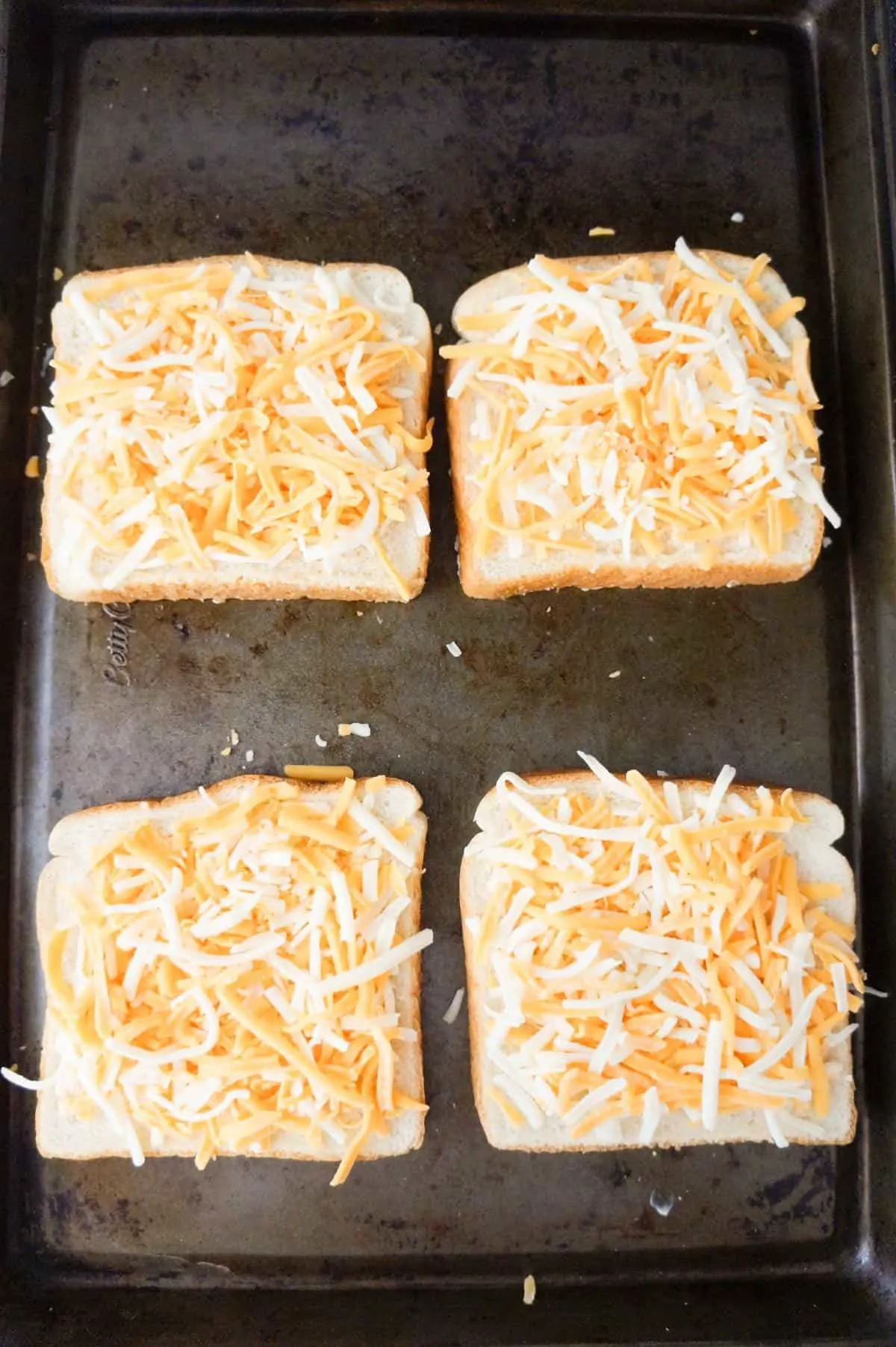 shredded cheddar cheese on top of bread on a baking sheet
