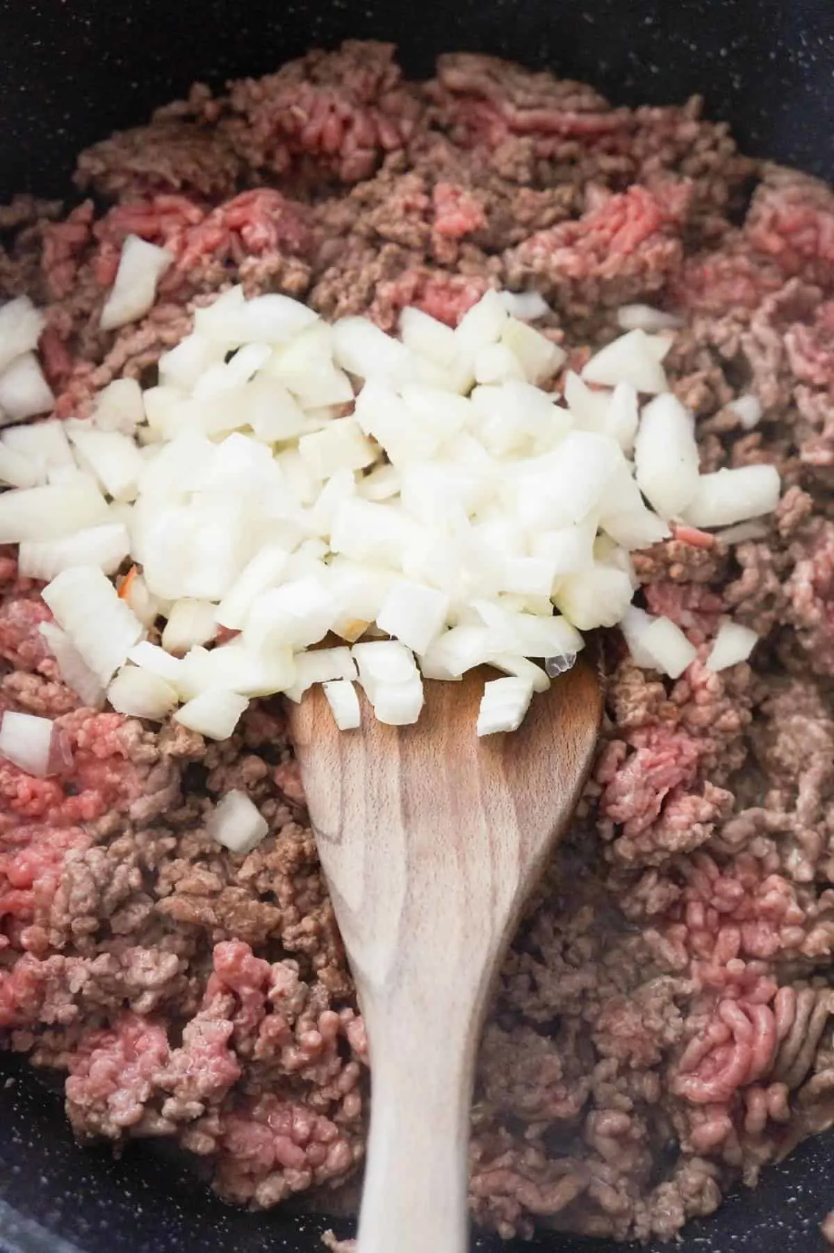 diced onions on top of ground beef cooking in a large saute pan