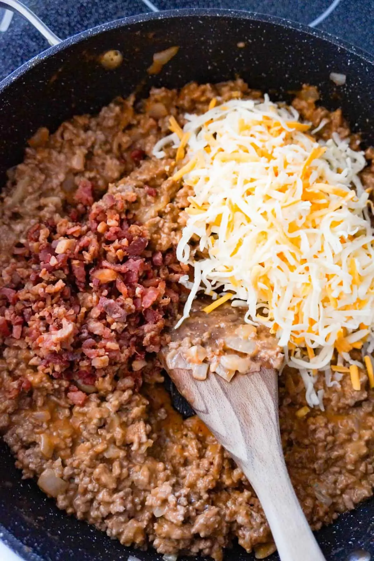 crumbled bacon and shredded cheese on top of ground beef mixture in a large saute pan