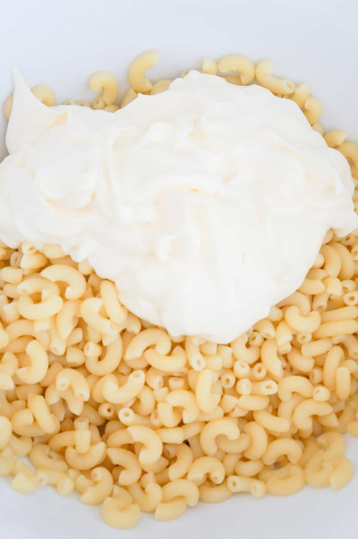 mayo on top of cooked macaroni noodles in a mixing bowl