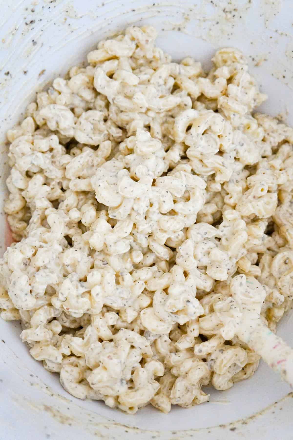 macaroni coated with mayo and basil pesto mixture in a mixing bowl