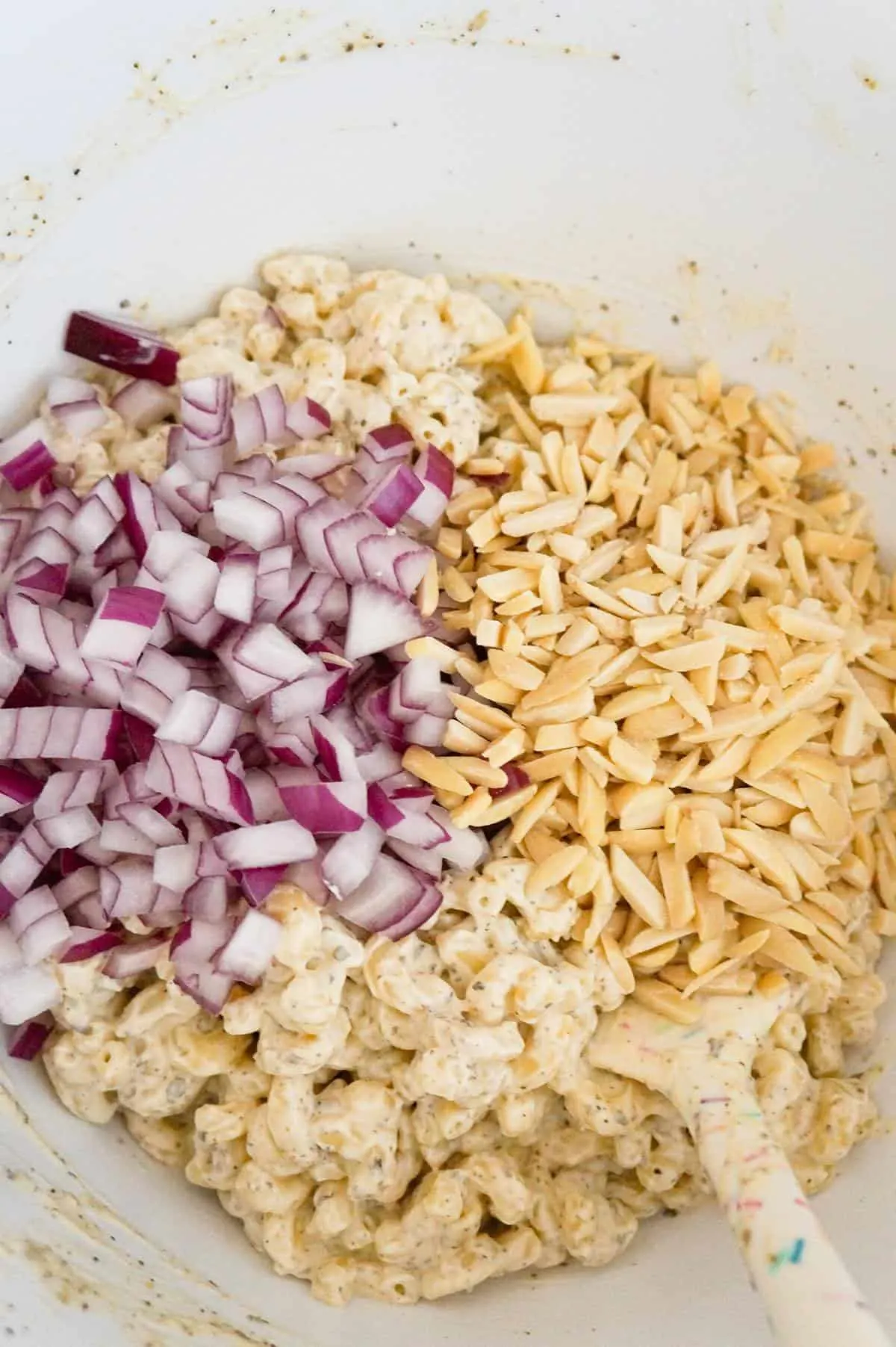 diced red onions and slivered almonds on top of macaroni salad in a mixing bowl