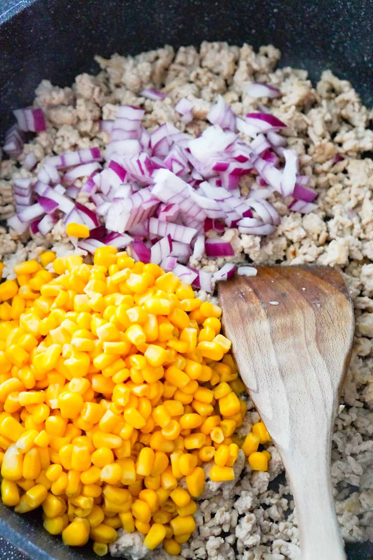 corn and diced red onions on top of cooked ground chicken in a saute pan