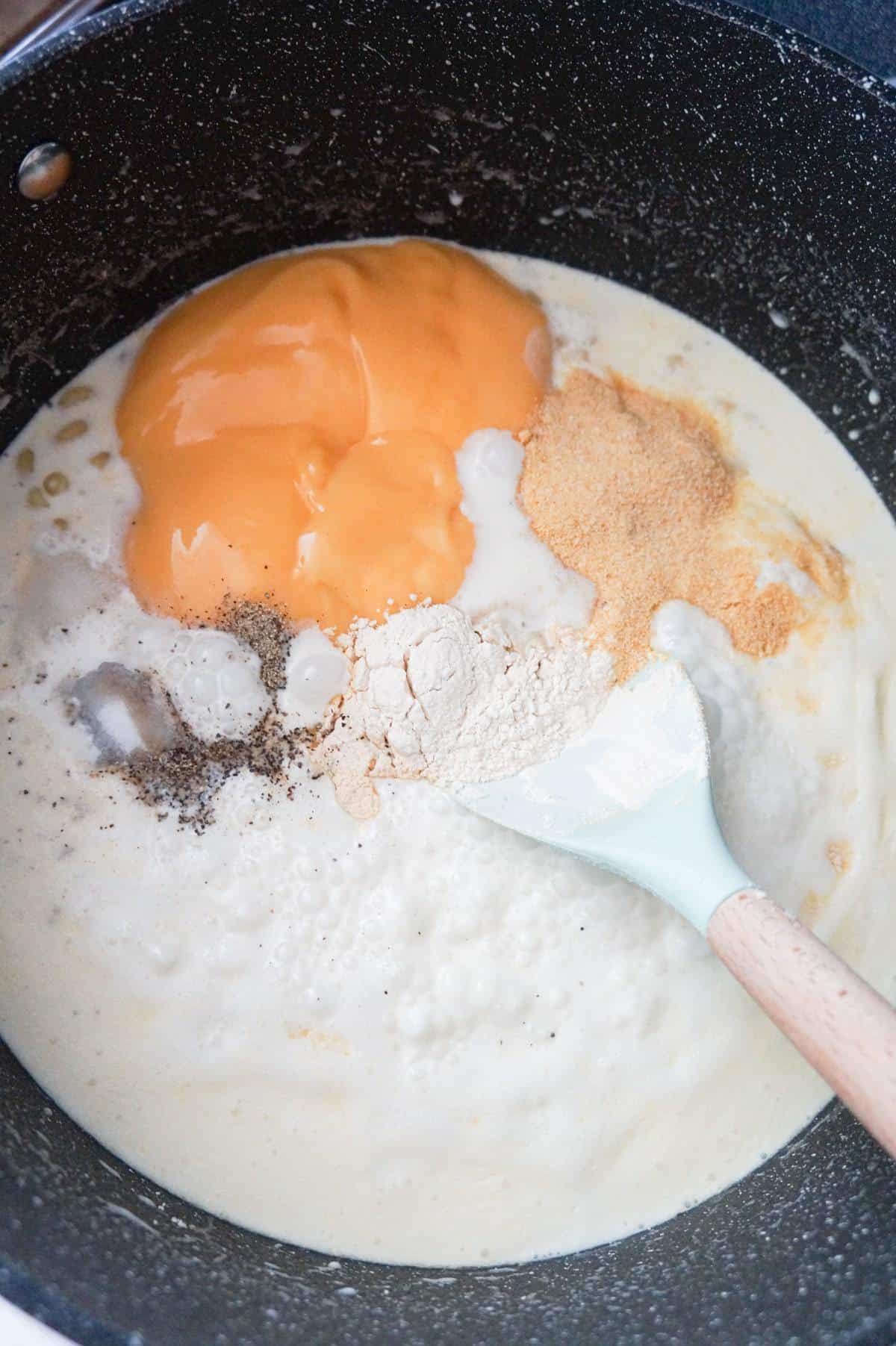 spices and condensed cheddar cheese soup on top of creamy macaroni in a large pot