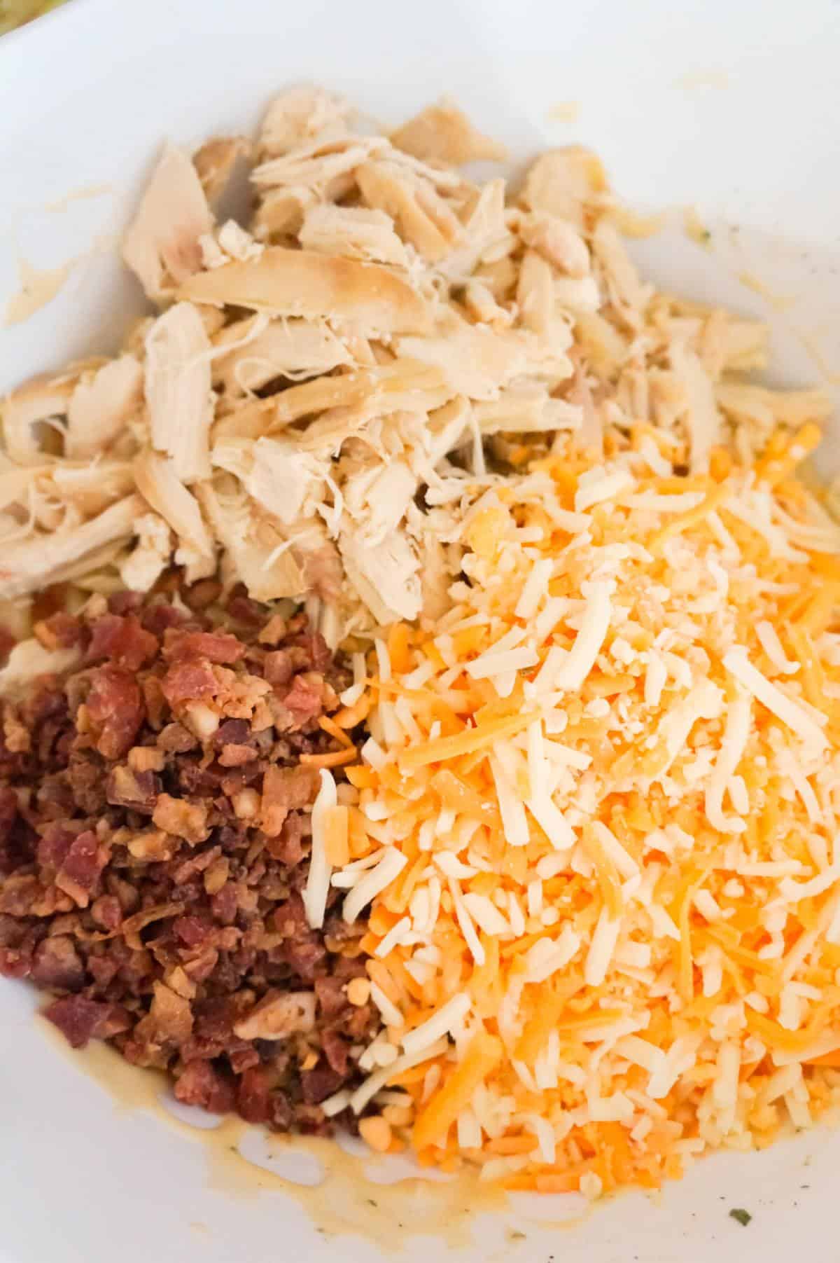 shredded chicken, crumbled bacon and shredded cheddar cheese on top of penne pasta in a mixing bowl