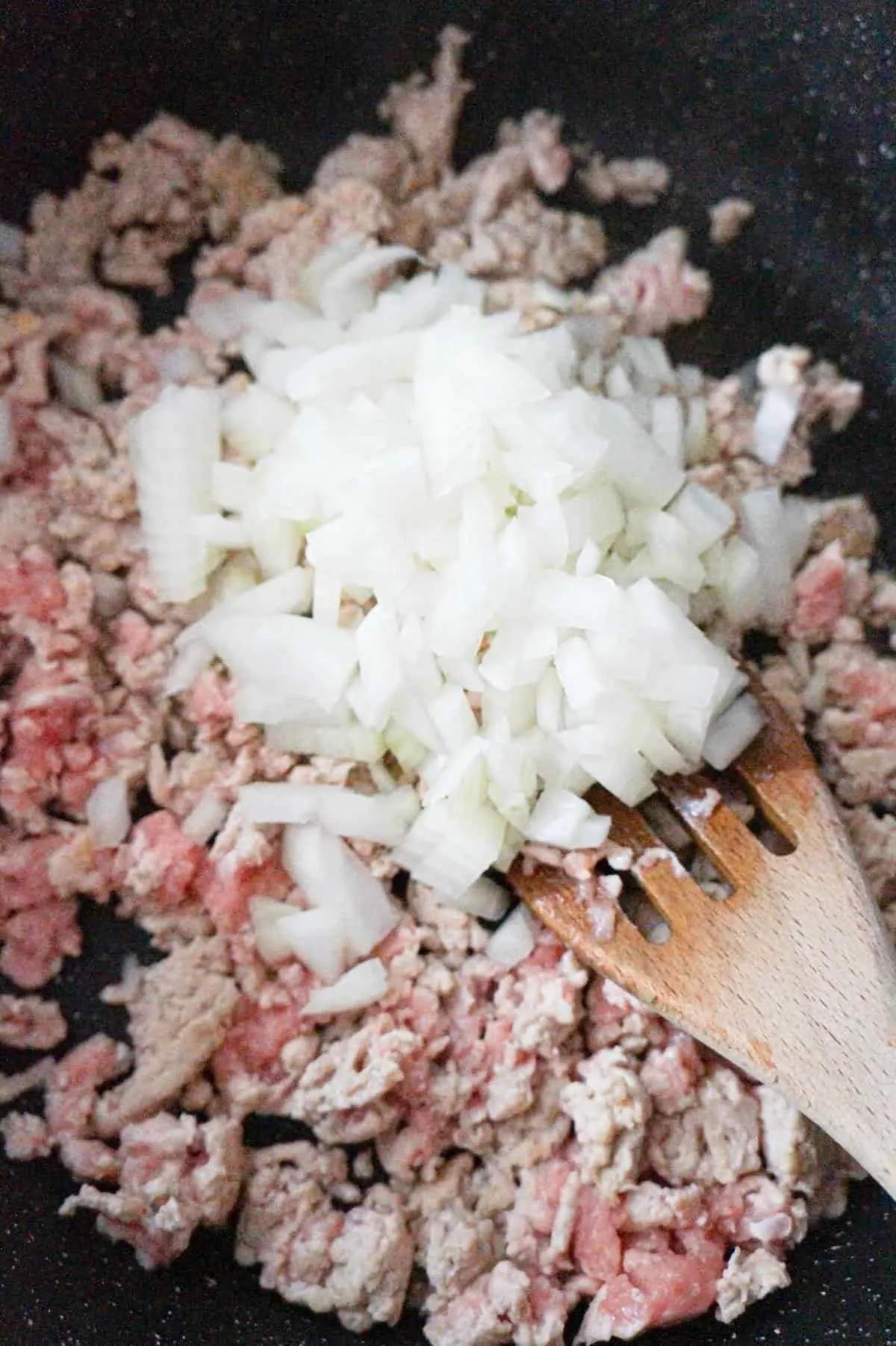 diced onions on top of ground chicken cooking in a saute pan