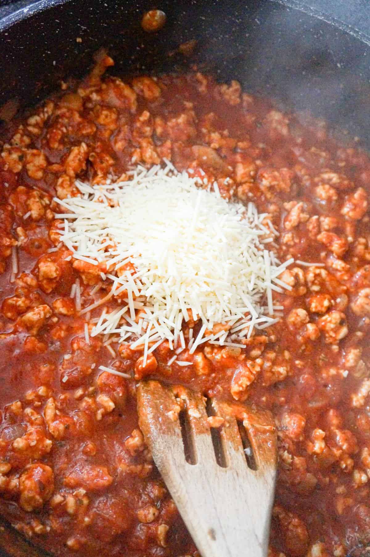 shredded Parmesan cheese on top of ground chicken and marinara mixture in a saute pan