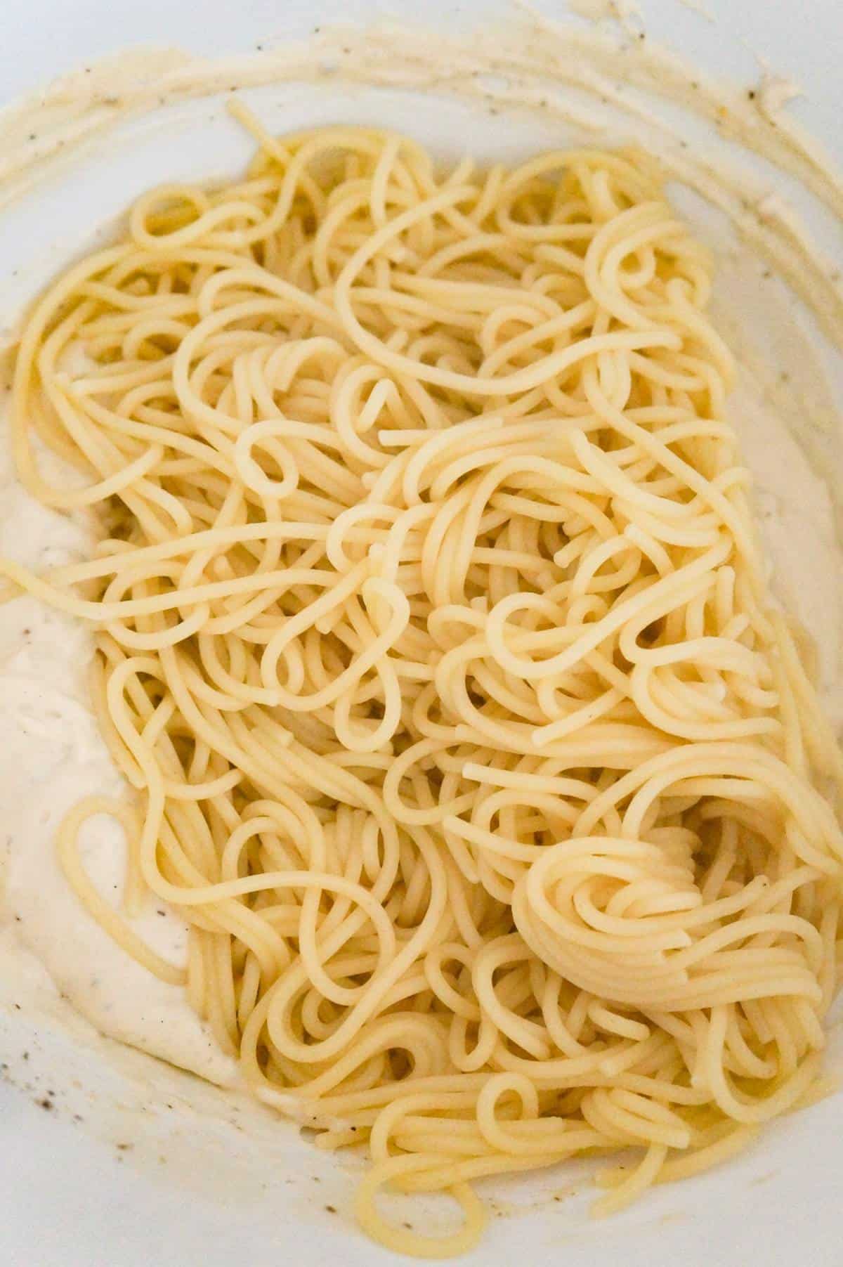 cooked spaghetti on top of creamy soup mixture in a mixing bowl