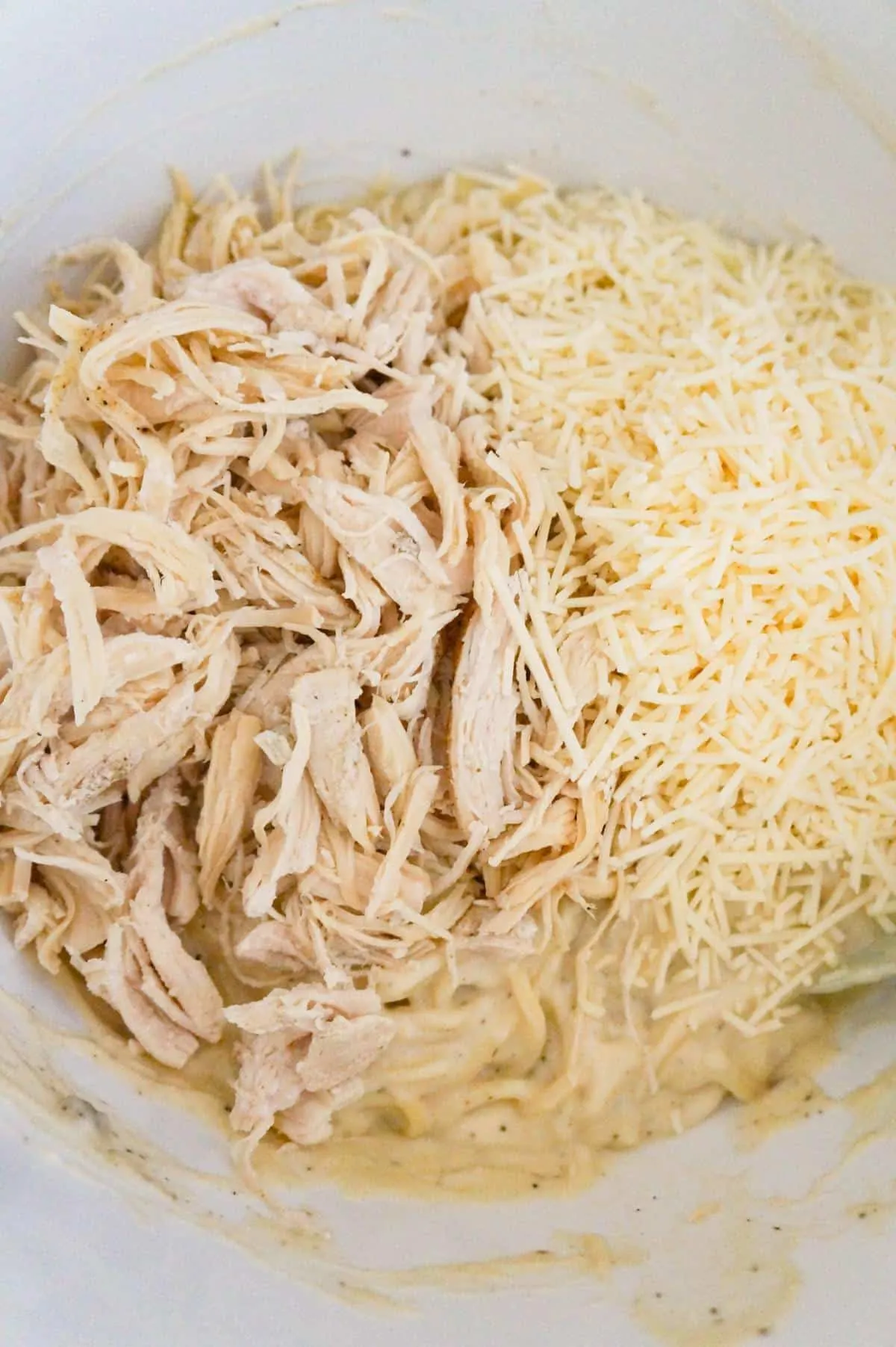shredded chicken and shredded Parmesan on top of spaghetti in a mixing bowl