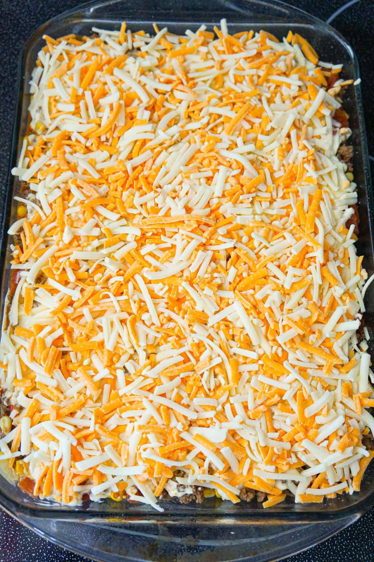 shredded cheddar and mozzarella cheese on top of beef and and biscuit casserole before baking