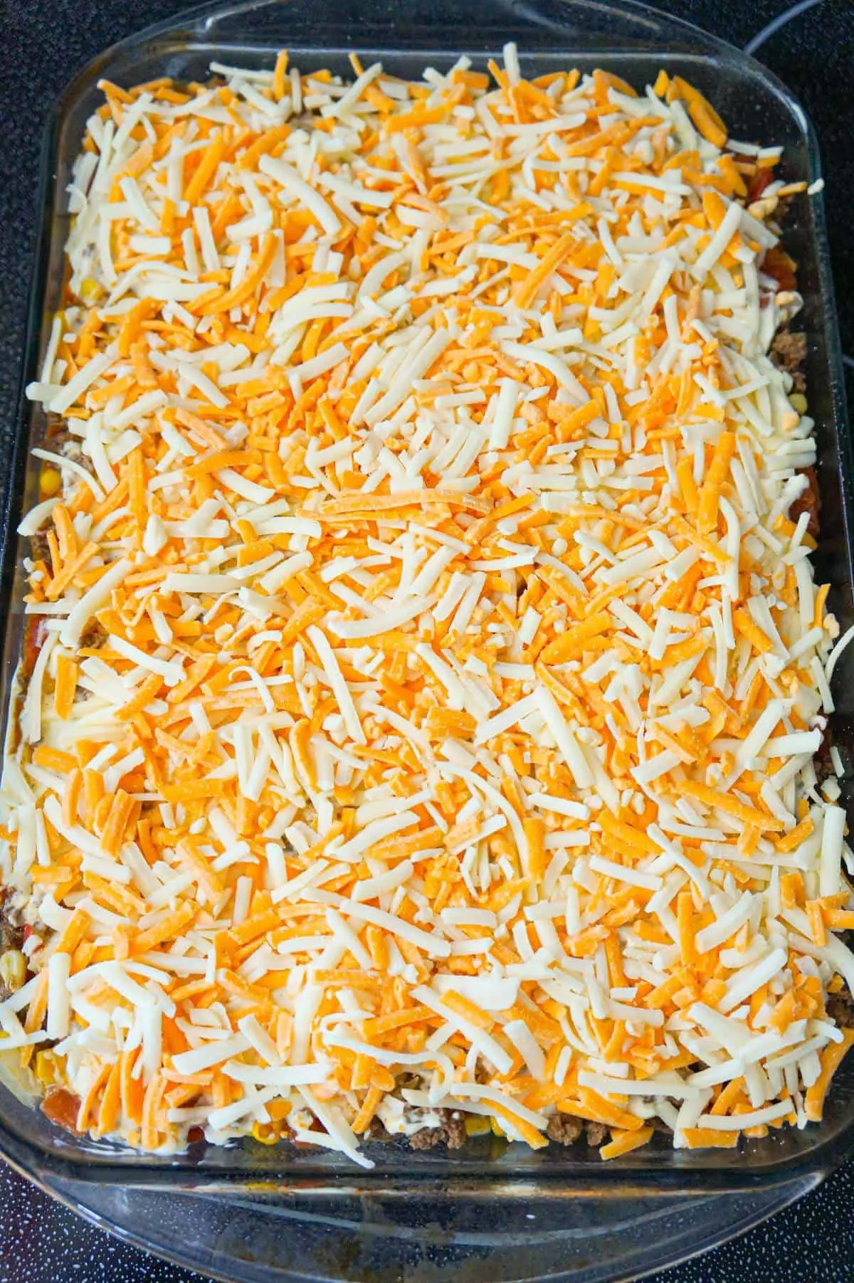 shredded cheddar and mozzarella cheese on top of beef and and biscuit casserole before baking
