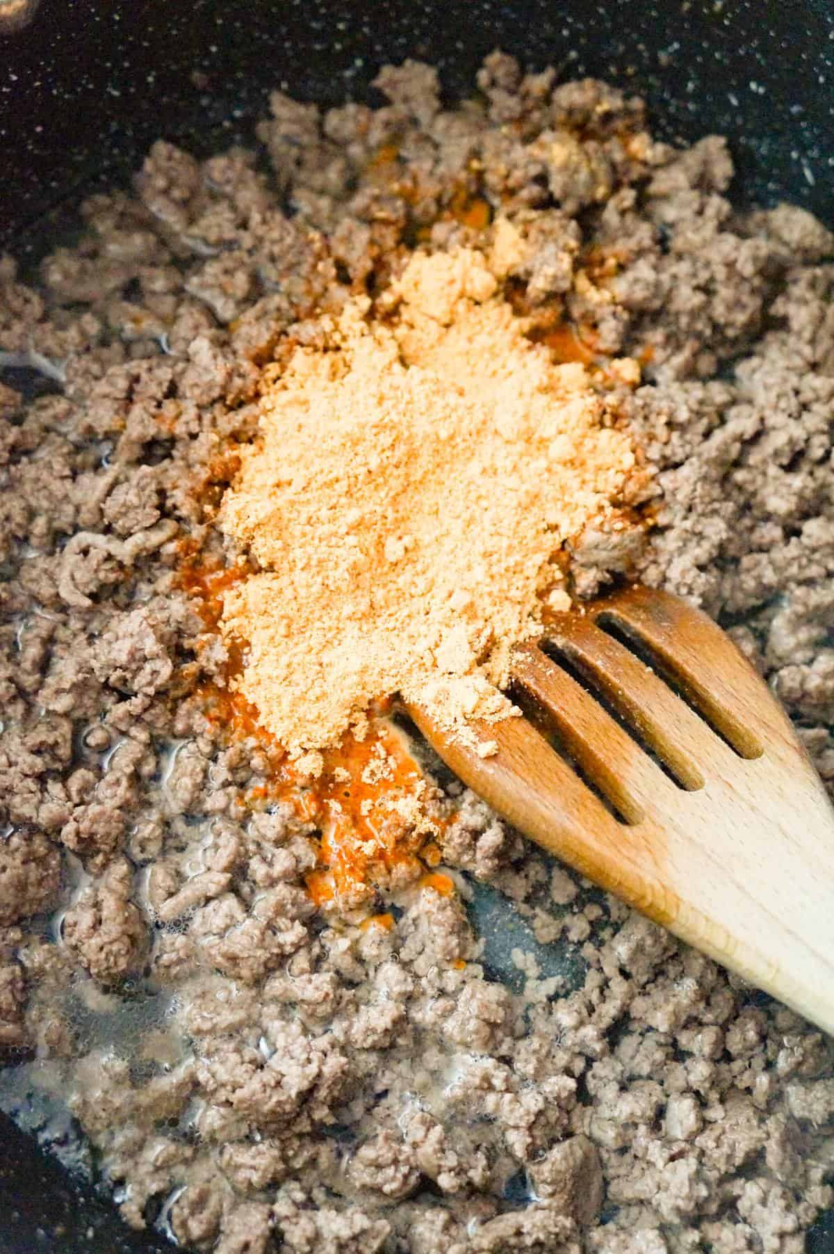 taco seasoning on top of cooked ground beef in a large saute pan