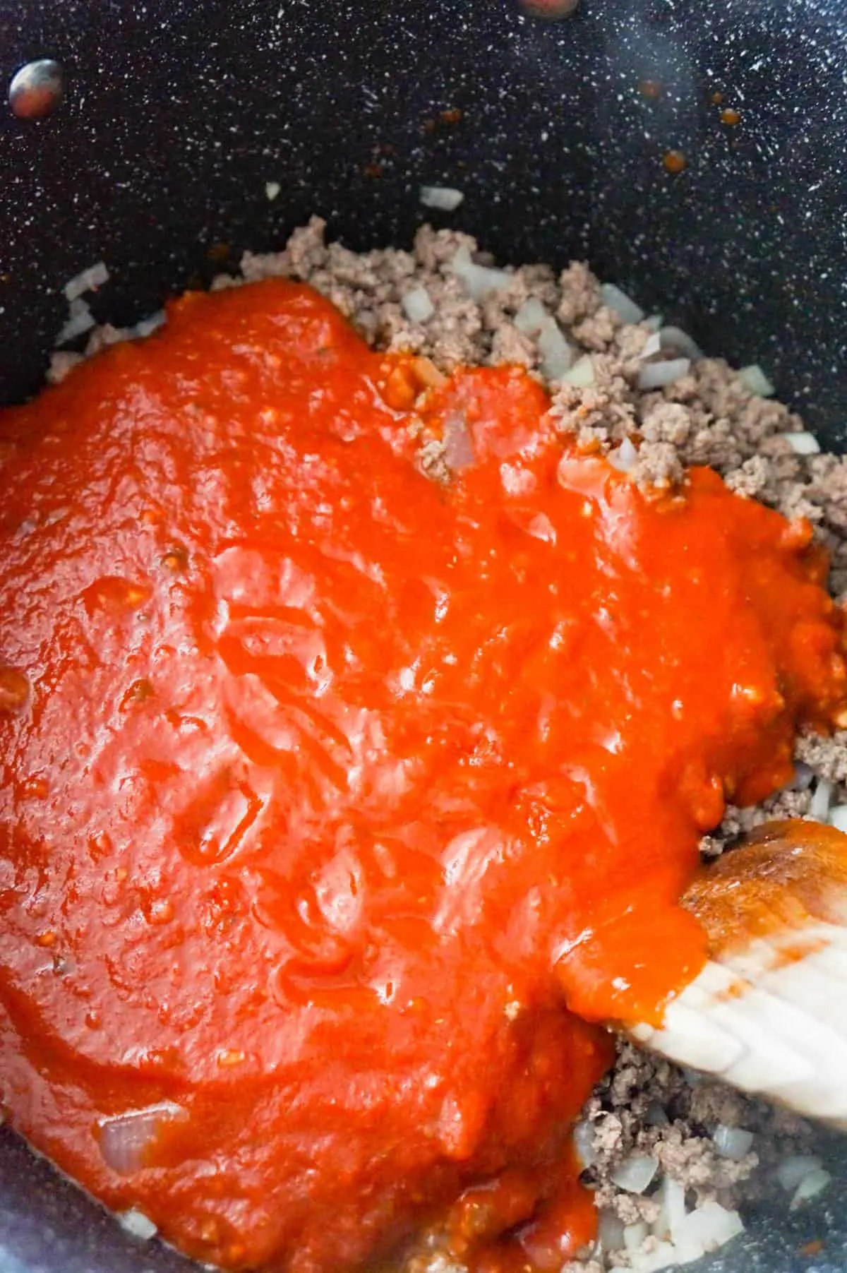 marinara sauce on top of cooked ground beef in a large pot