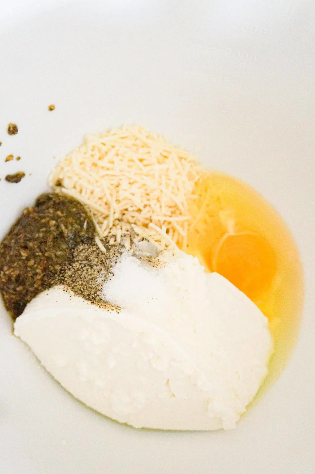 basil pesto, shredded parmesan, ricotta and an egg in a mixing bowl