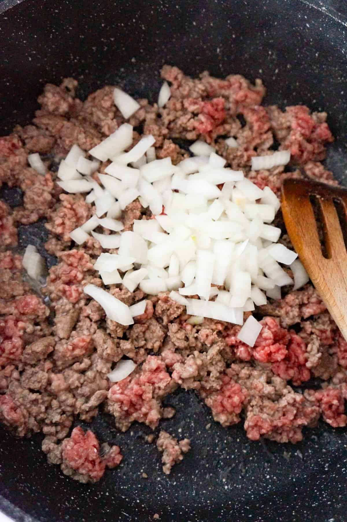 diced onions on top of ground beef in a saute pan