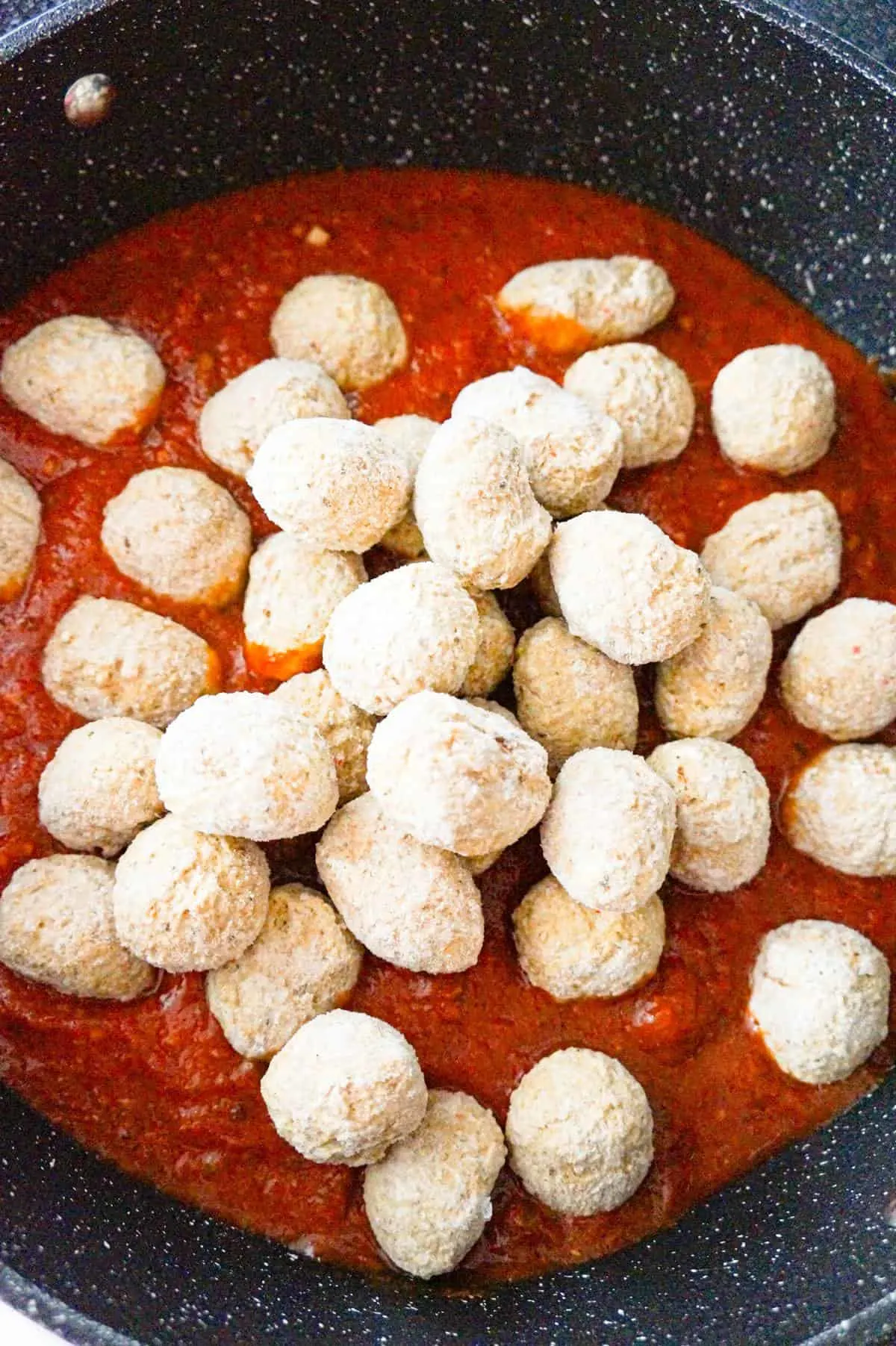 frozen meatballs on top of marinara sauce in a saute pan