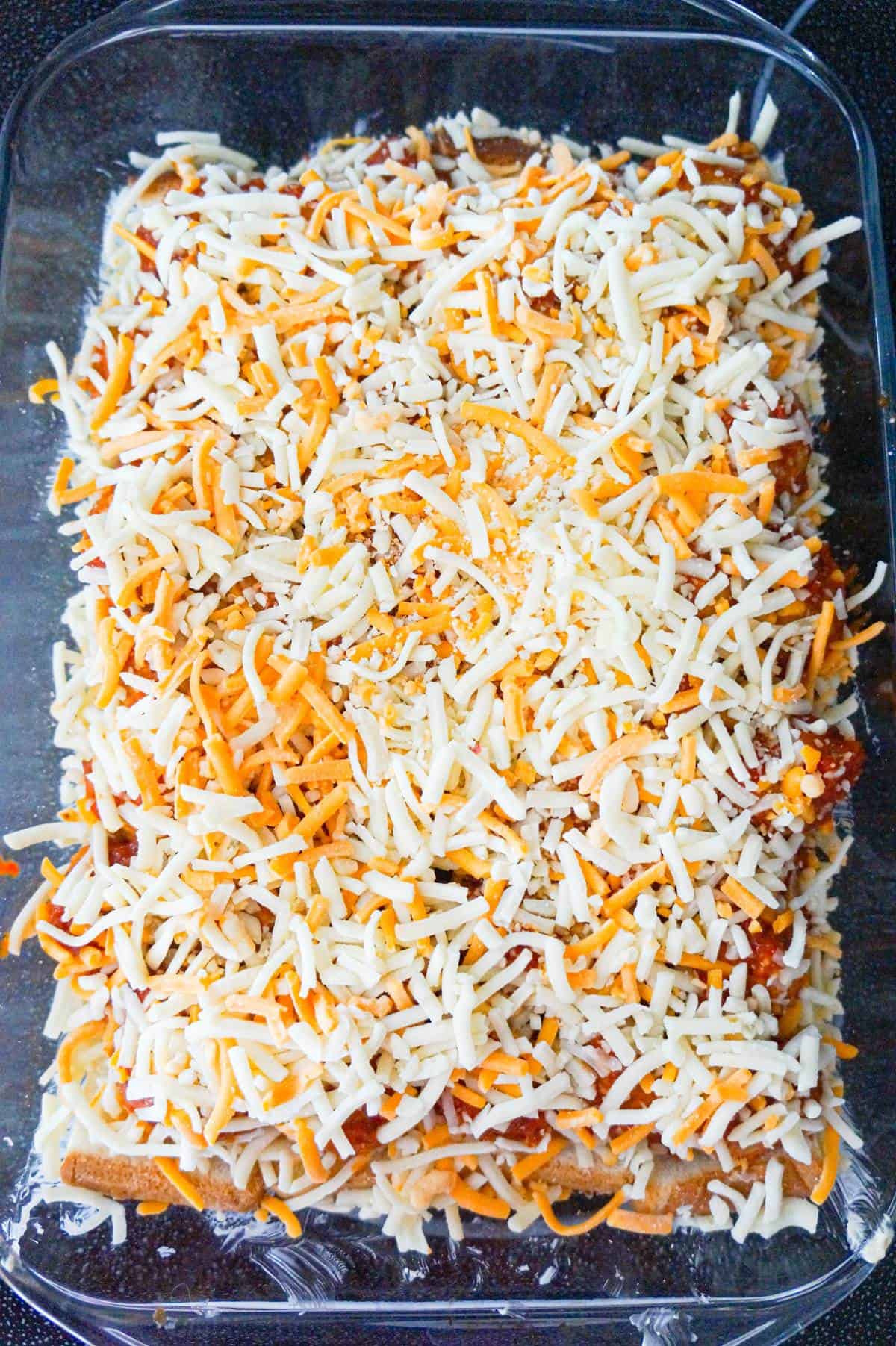 shredded mozzarella and cheddar cheese on top of meatball casserole in a baking dish