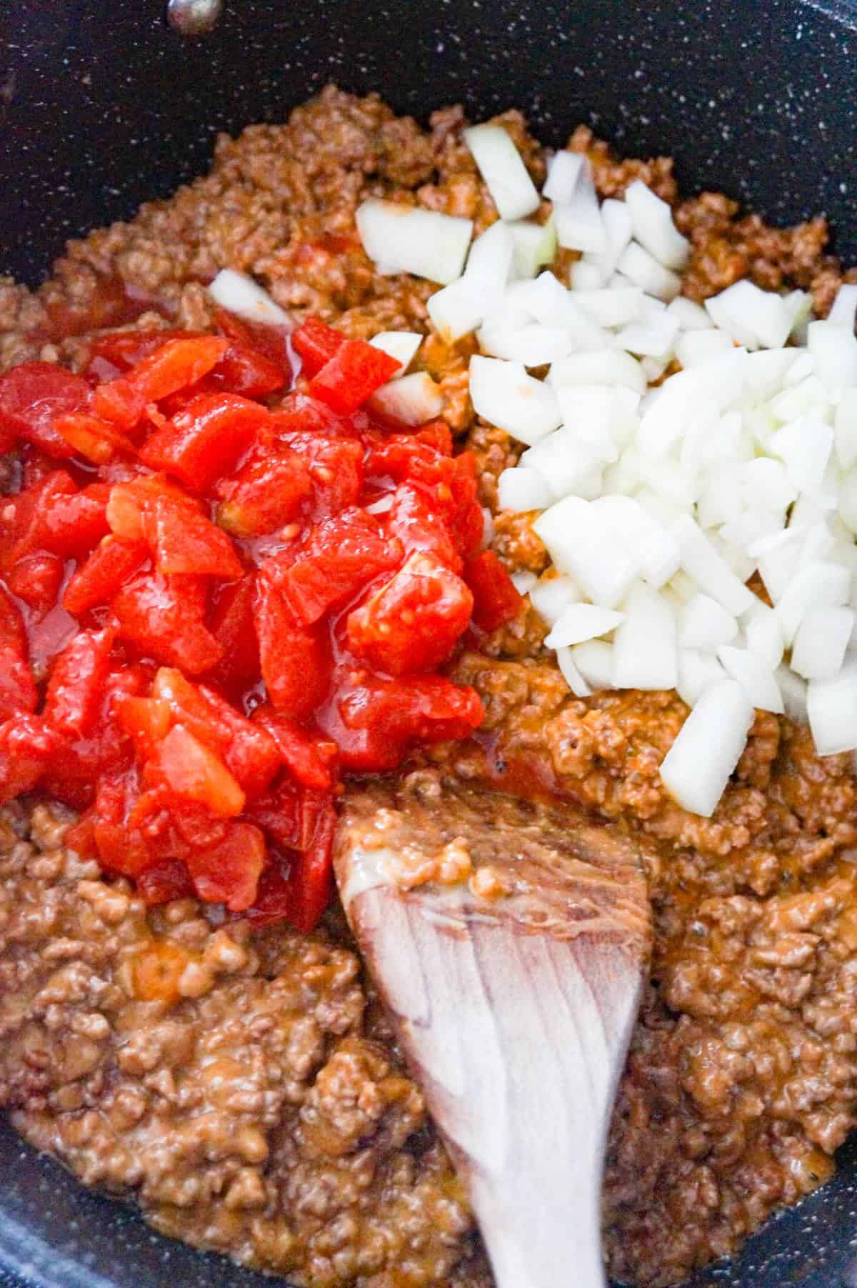 diced tomatoes and diced onions on top of ground beef mixture in a saute pan