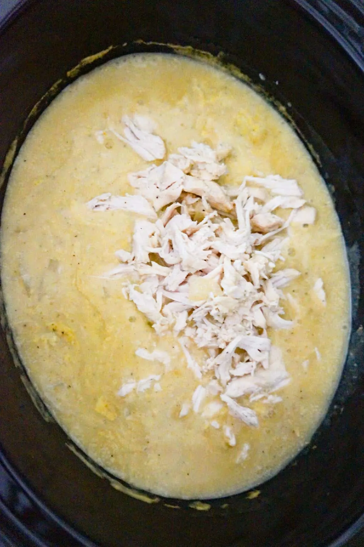 cooked shredded chicken on top of creamy chicken sauce mixture in a slow cooker
