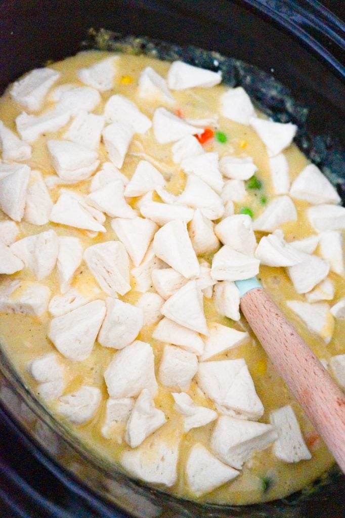 Pillsbury biscuit dough pieces on top of creamy chicken mixture in a slow cooker