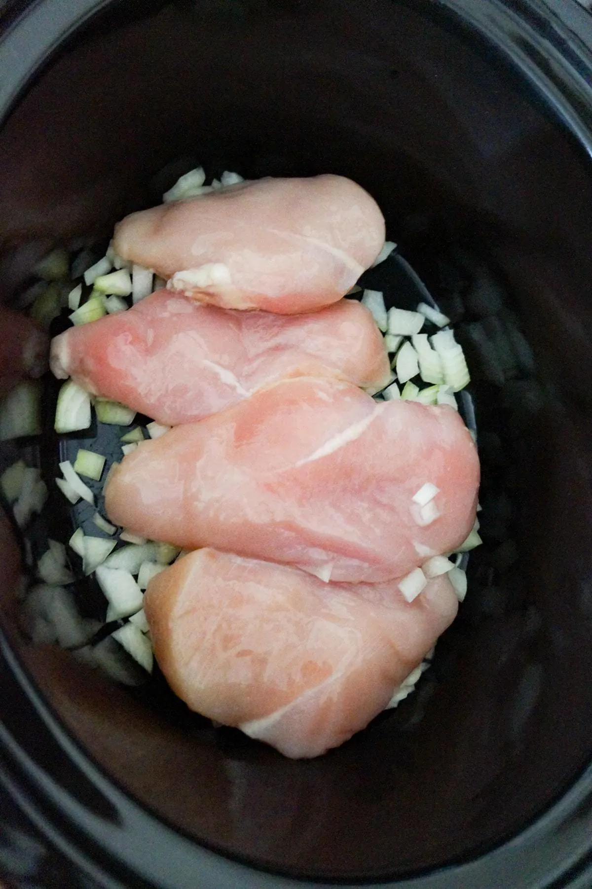 raw chicken breasts on top of diced onion in a crock pot