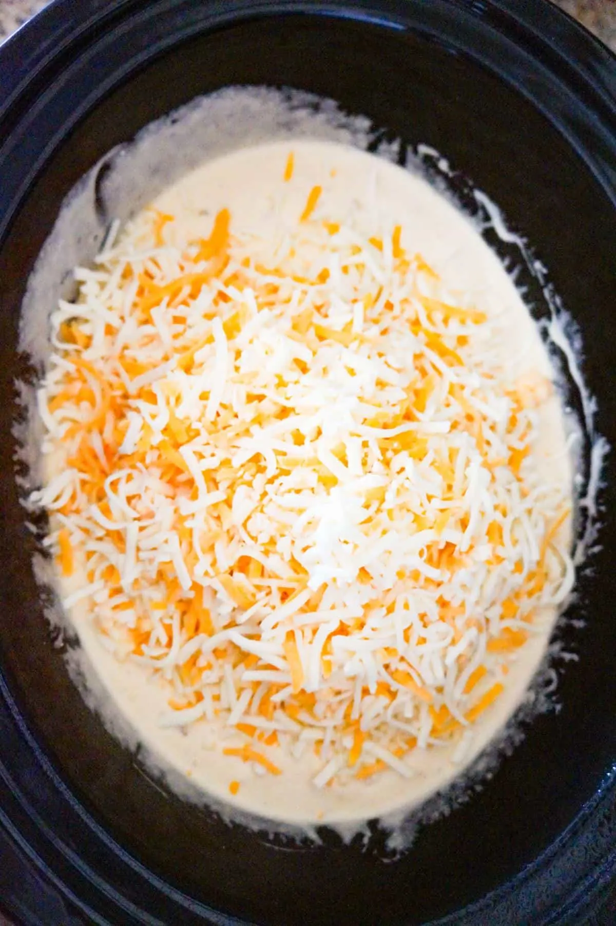 shredded mozzarella and cheddar cheese on top of mac and cheese in a crock pot before cooking
