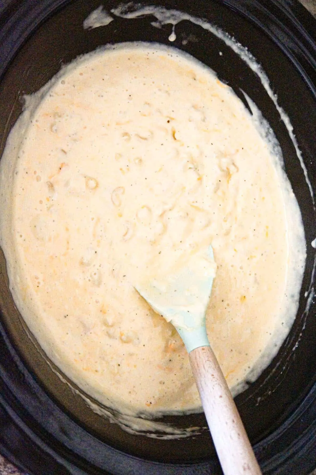 mac and cheese in a crock pot being stirred part way through cooking