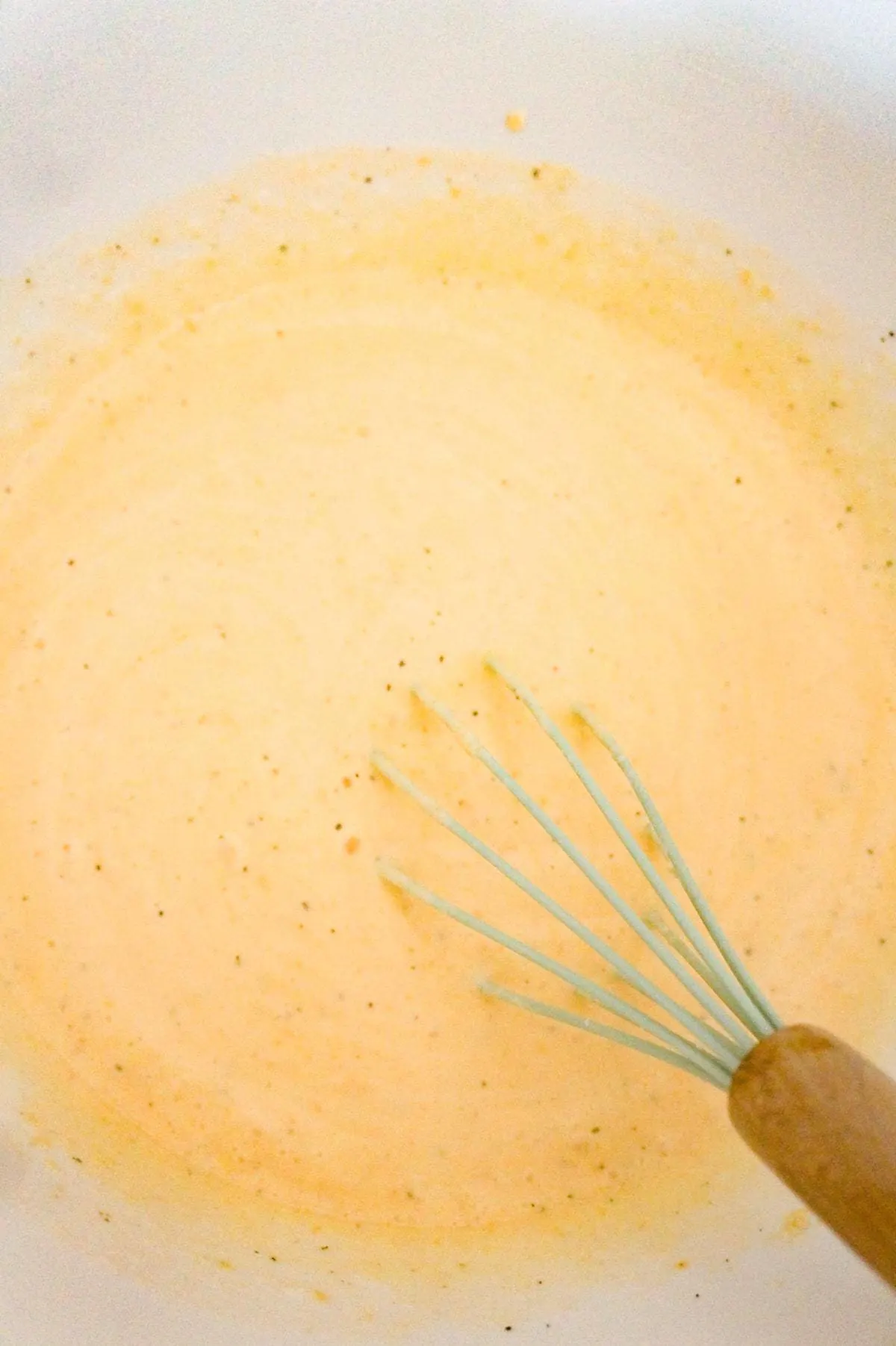 creamy cheddar soup mixture being stirred in a mixing bowl