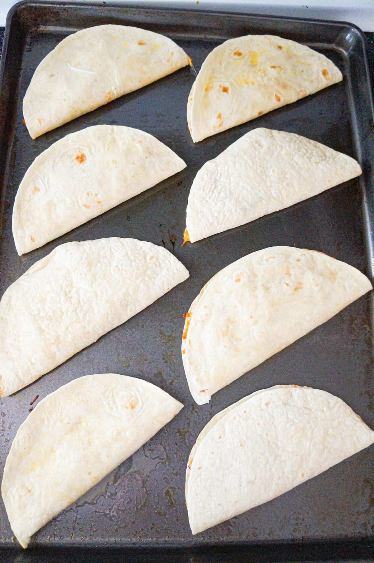 chicken quesadillas on a baking sheet before flipping