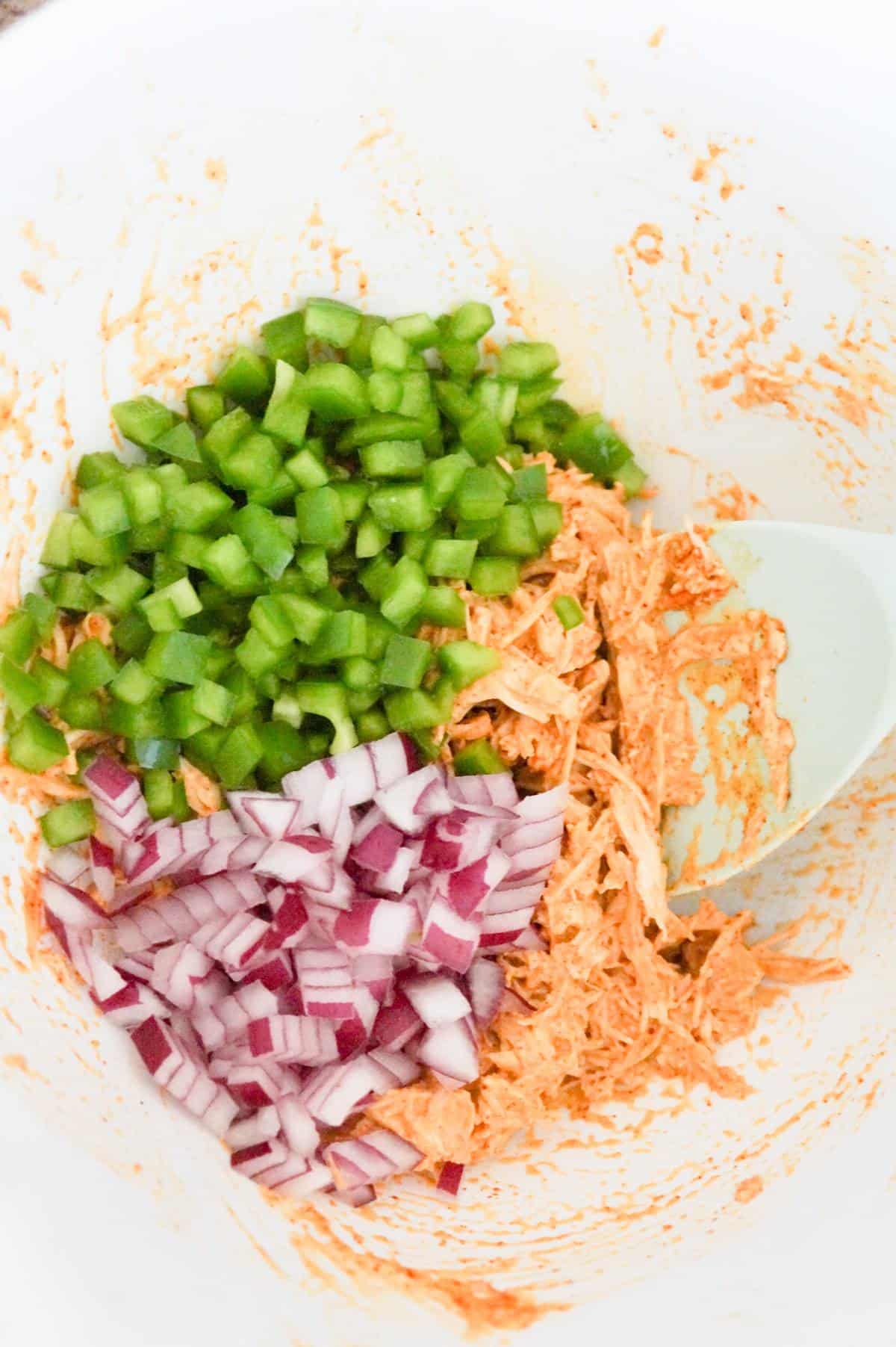 diced green peppers and diced red onions on top of chicken taco mixture in a mixing bowl