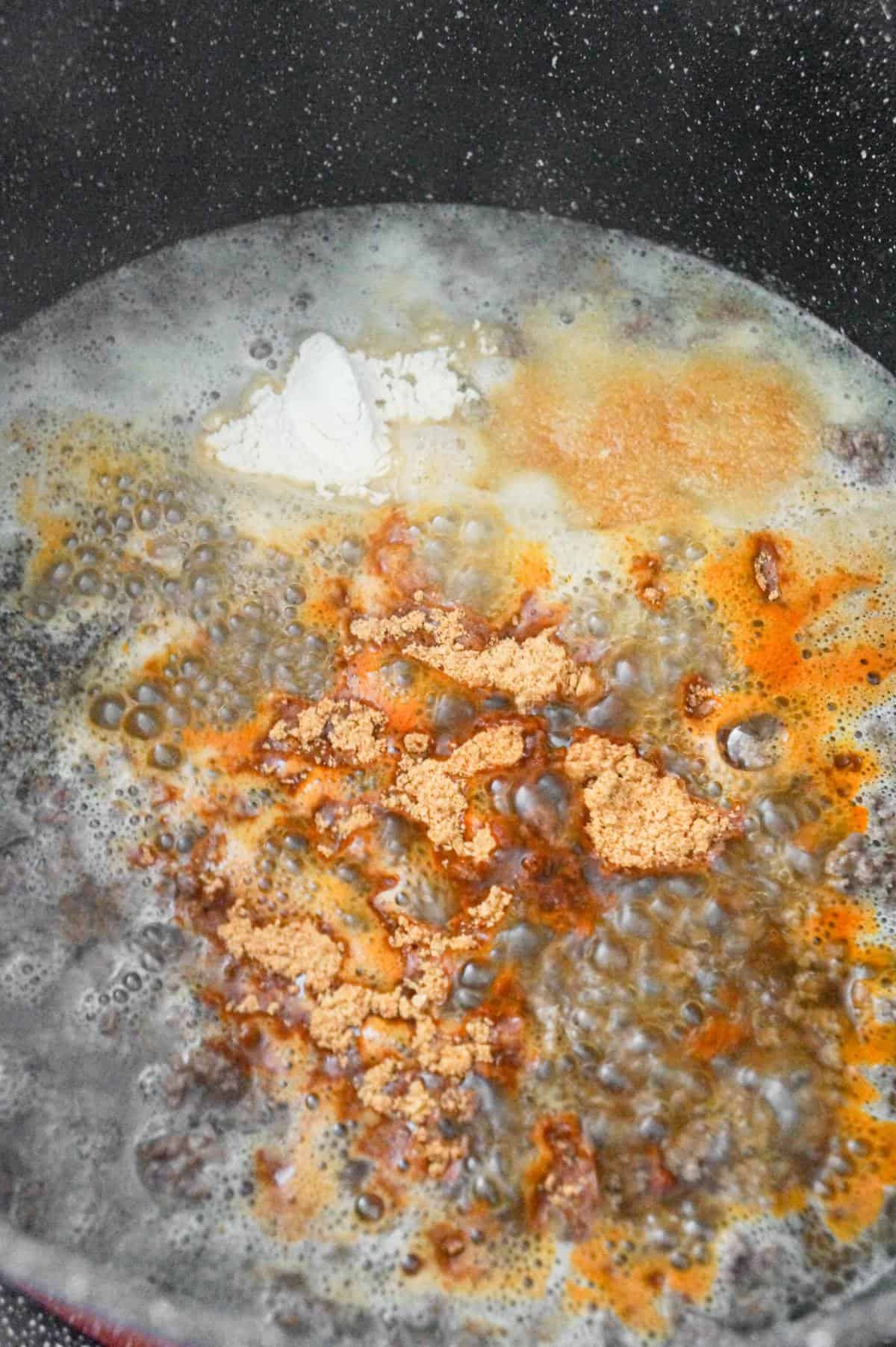 taco seasoning and spices on top of water and ground beef mixture in a large pot