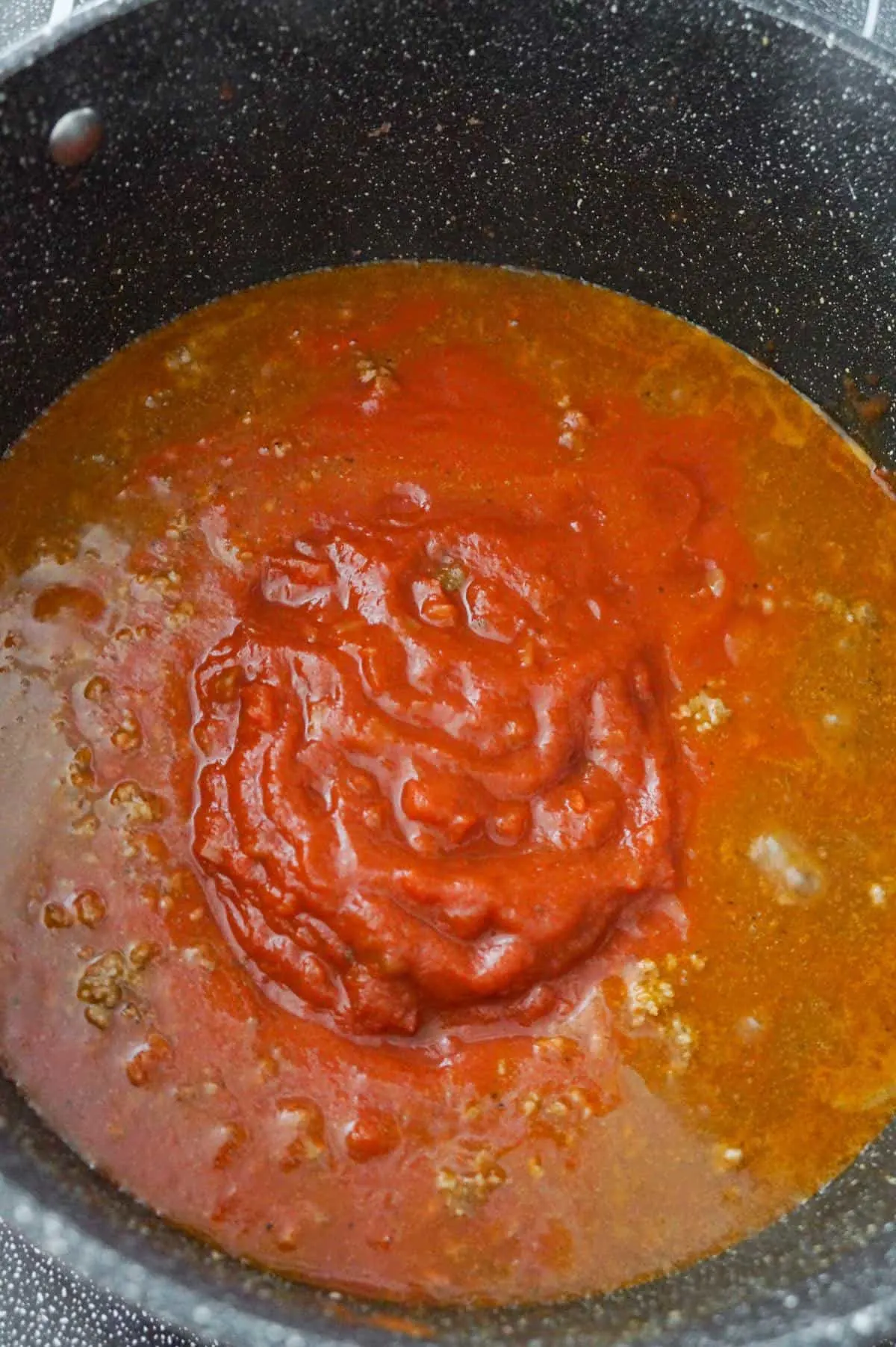 tomato sauce on top of ground beef and taco seasoning mixture in a large pot