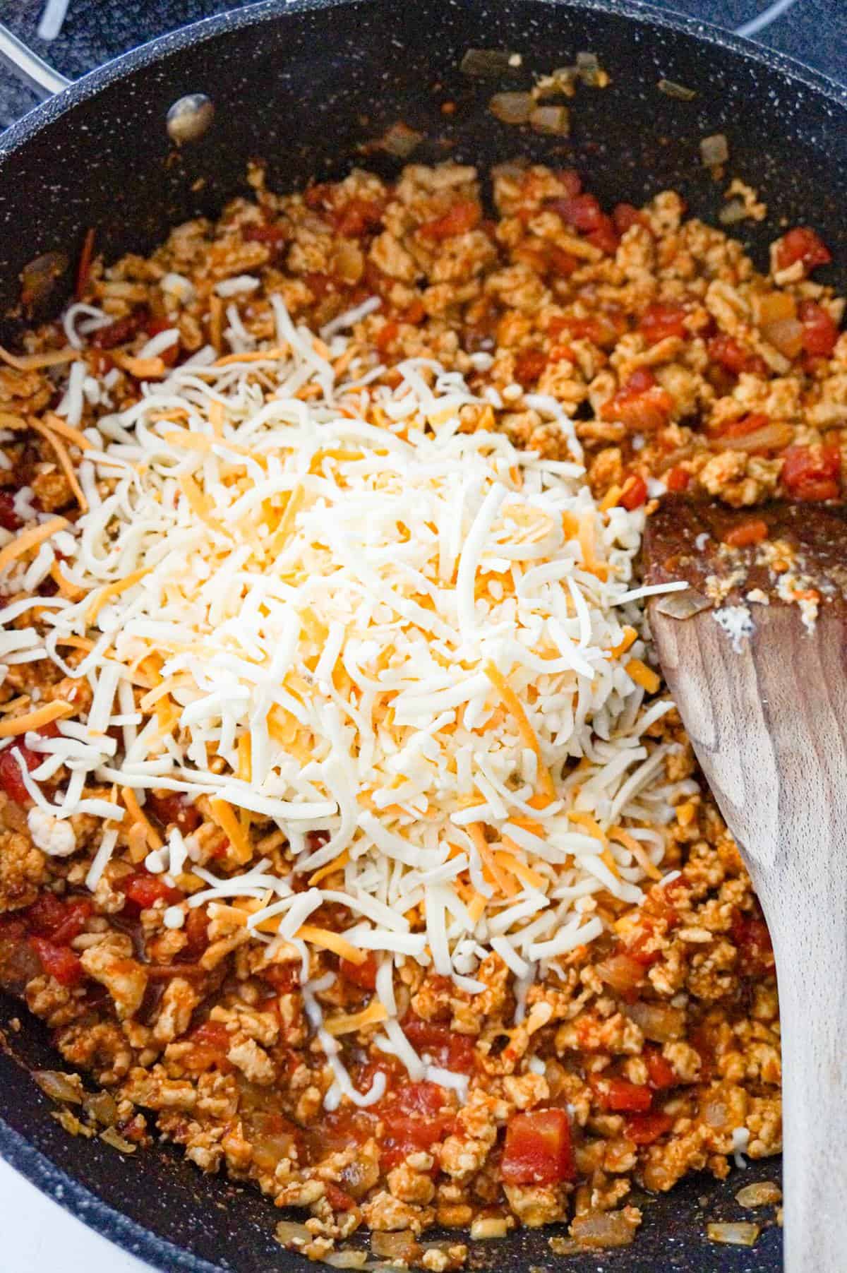 shredded cheese on top of ground chicken taco meat in a saute pan