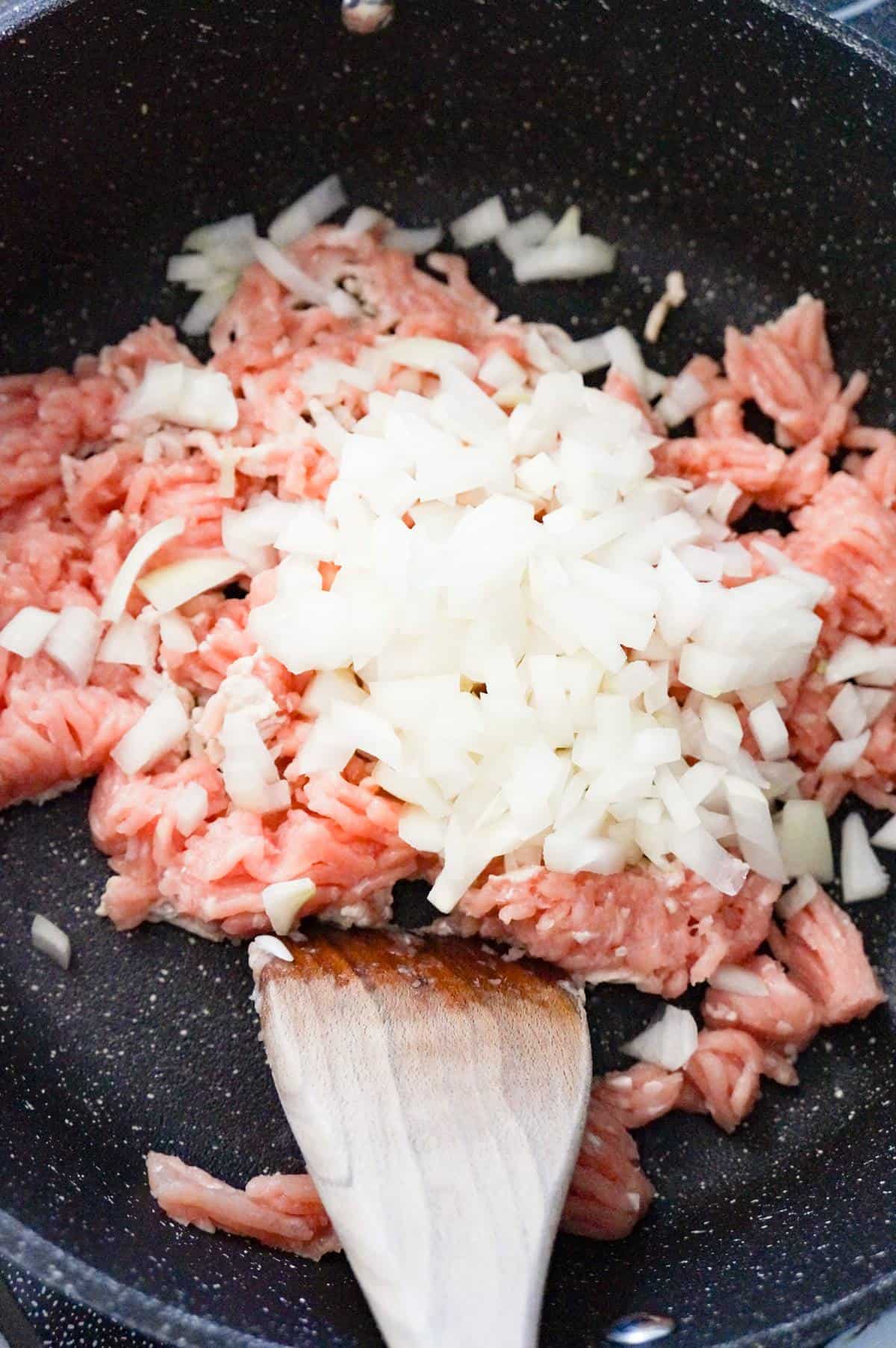 diced onions on top of raw ground chicken in a saute pan