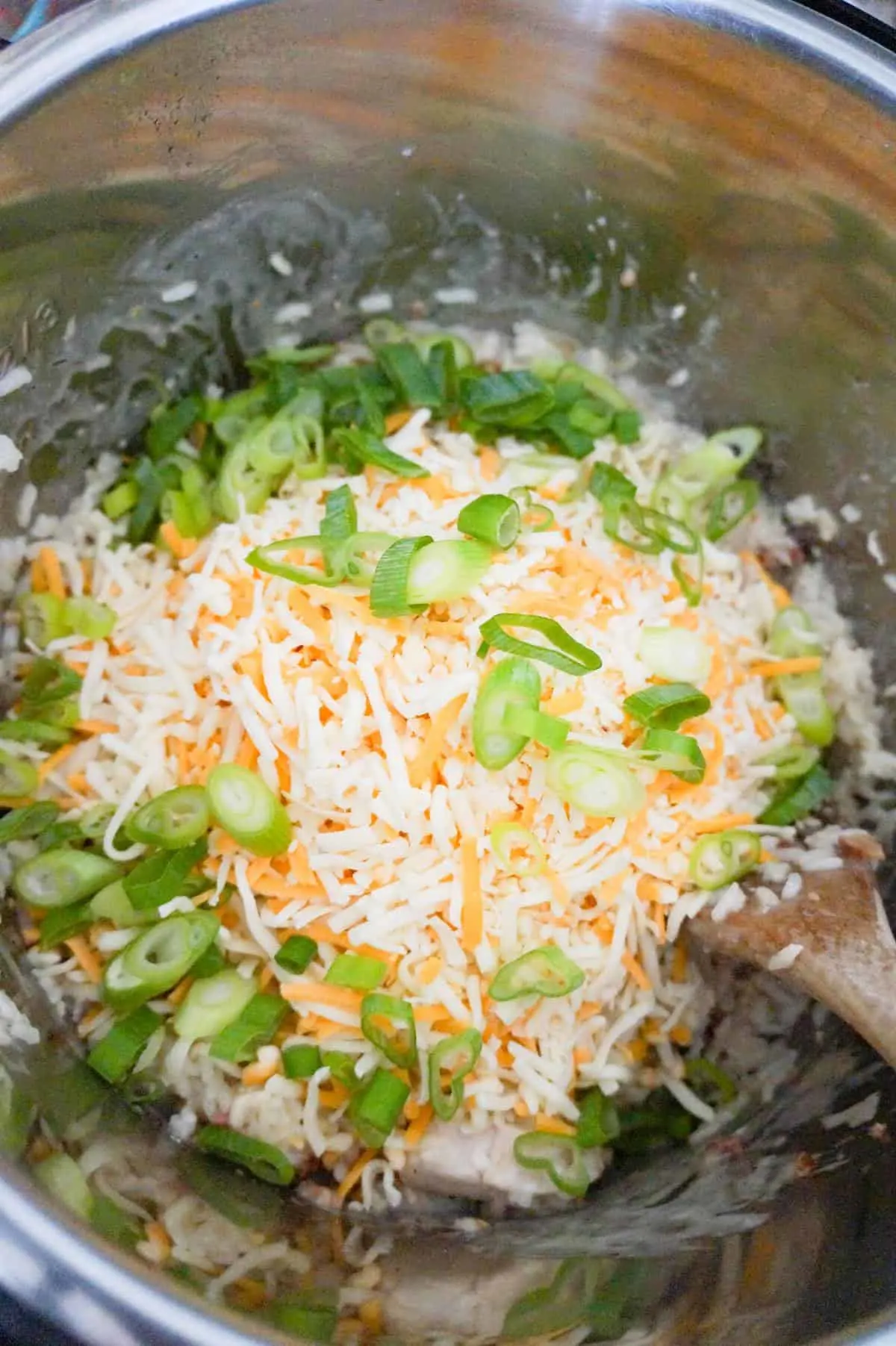 shredded cheddar cheese and chopped green onions on top of cooked chicken and rice in an Instant Pot