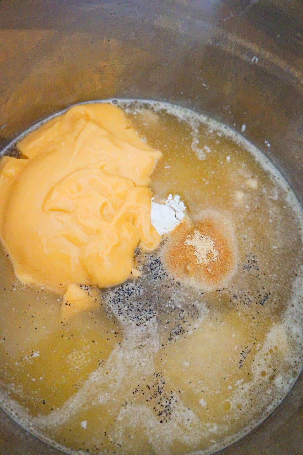 spices and condensed cheddar cheese soup on top of chicken breast chunks in broth in an Instant Pot