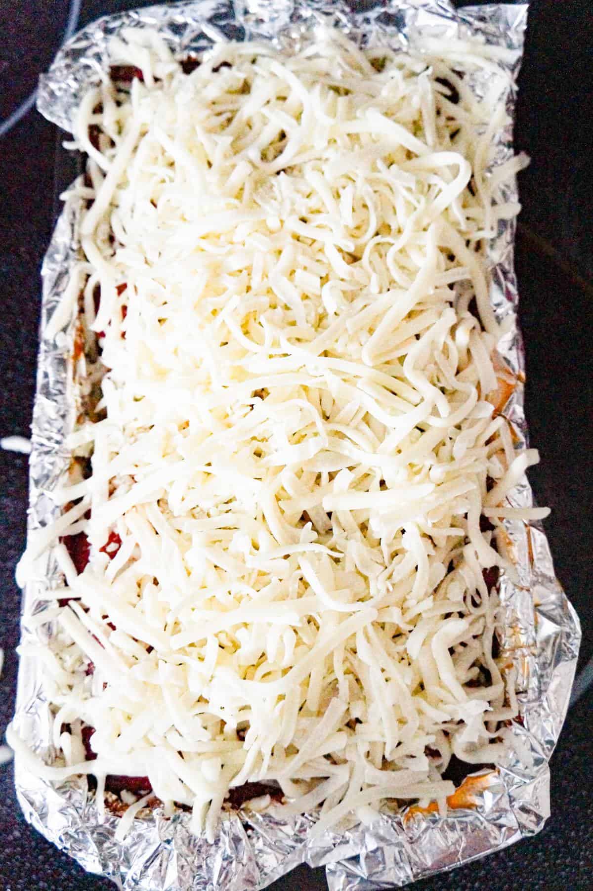 shredded Italian cheeses on top of meatloaf in a loaf pan