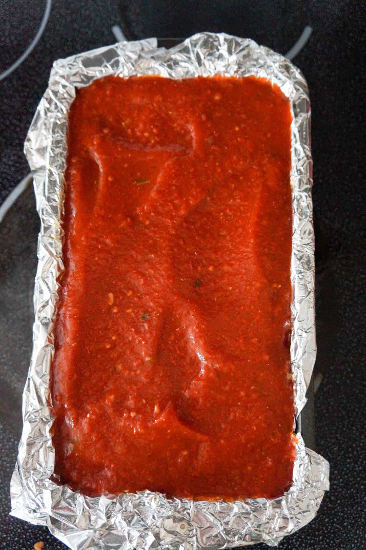 marinara sauce on top of meatloaf in a loaf pan before baking