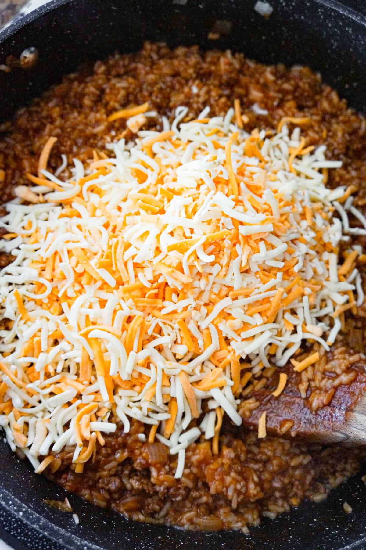 shredded mozzarella and cheddar cheese on top of ground beef and rice mixture in a saute pan