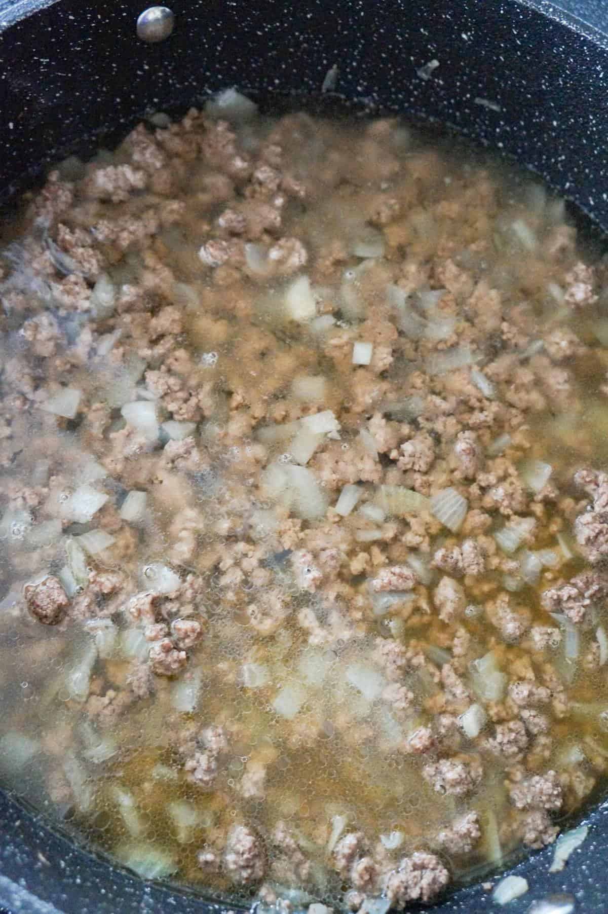 cooked ground beef and chicken broth in a saute pan
