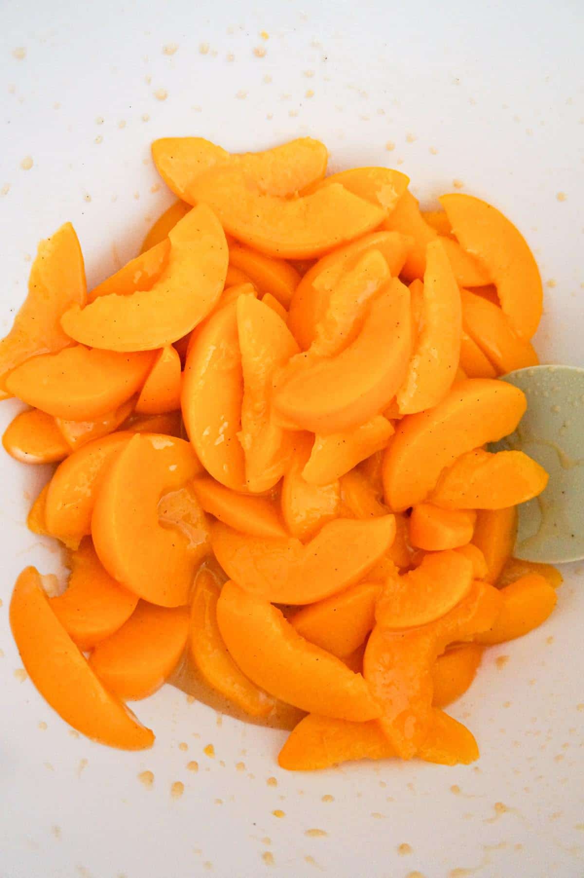 peach slices tossed in brown sugar and corn starch in a mixing bowl