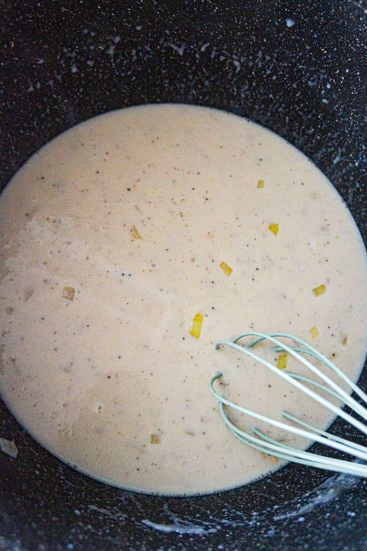 creamy onion sauce in a large pot with a whisk
