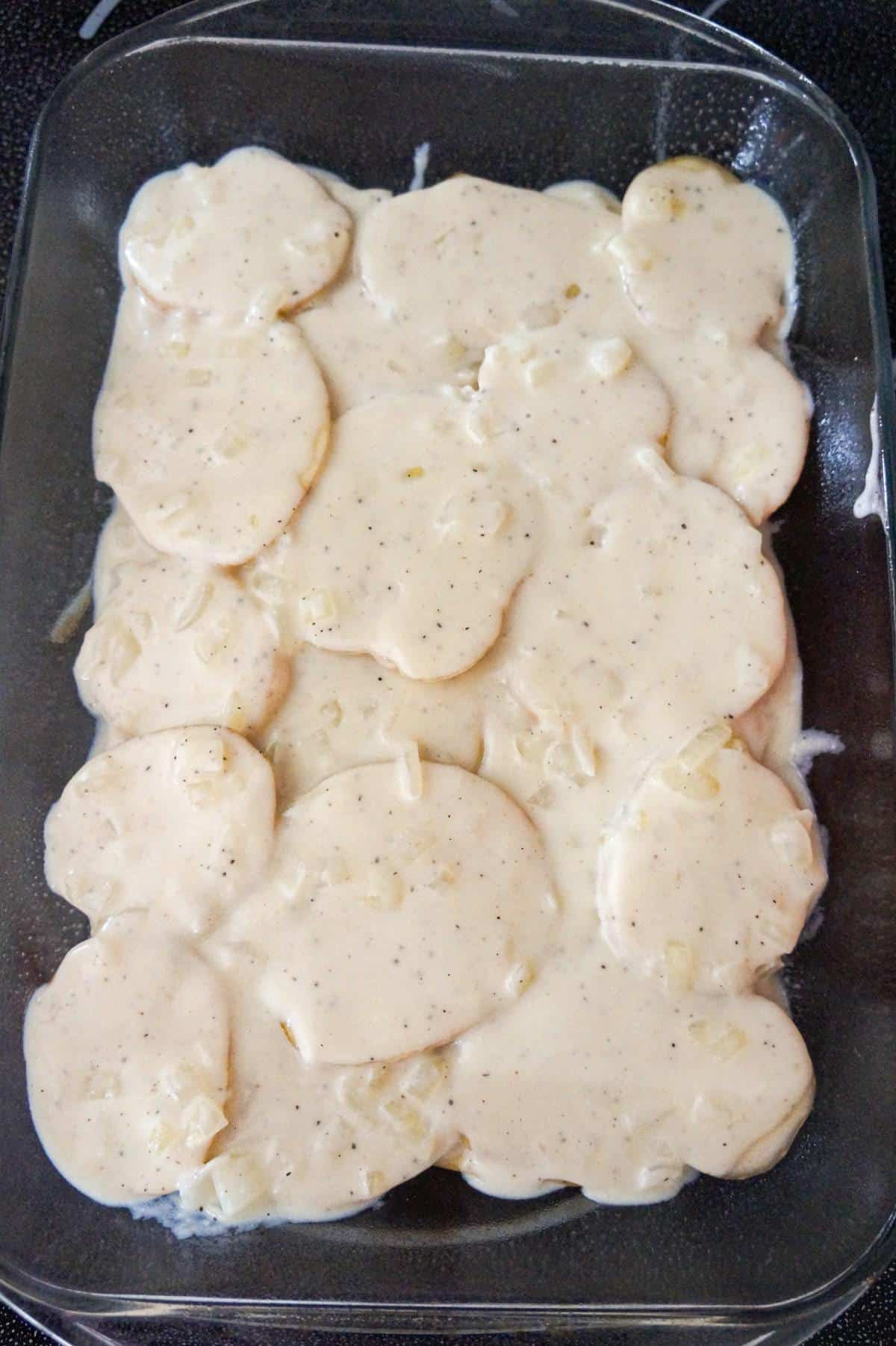 creamy onion sauce on top of sliced potatoes in a baking dish