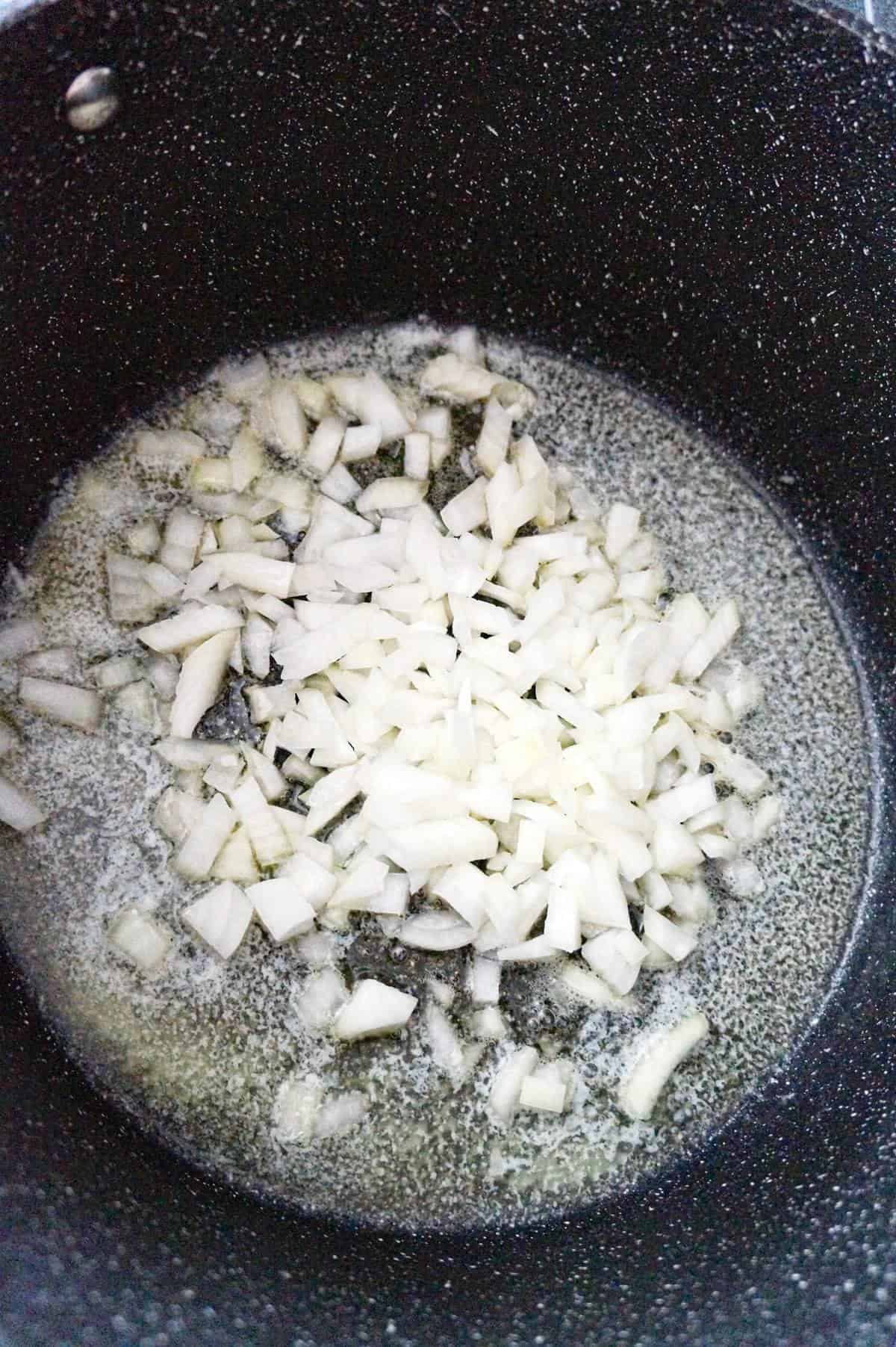 diced onions added to a large pot with melted butter