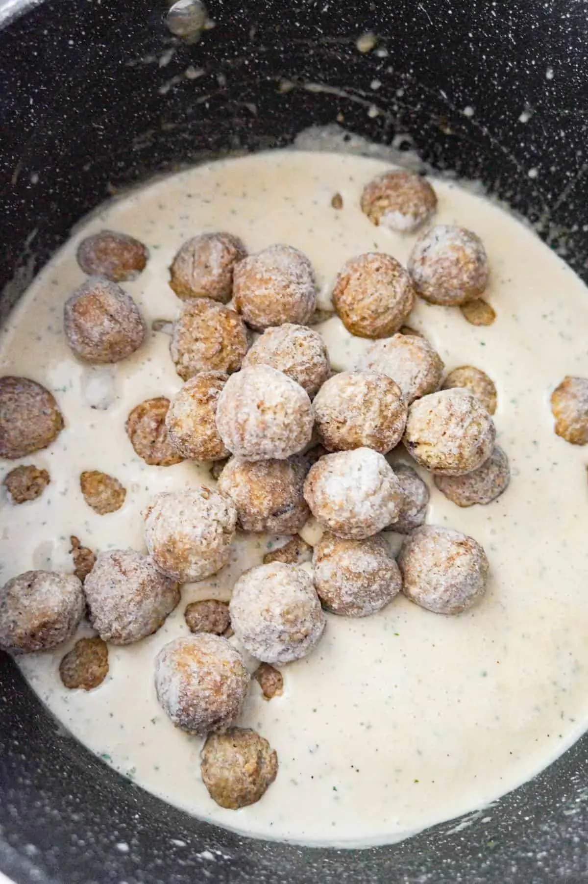frozen Swedish meatballs added to cream sauce in a large pot